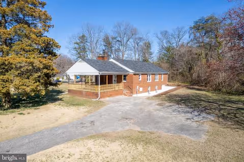 Brick one-story building with a covered front porch, gravel driveway, and surrounding trees.