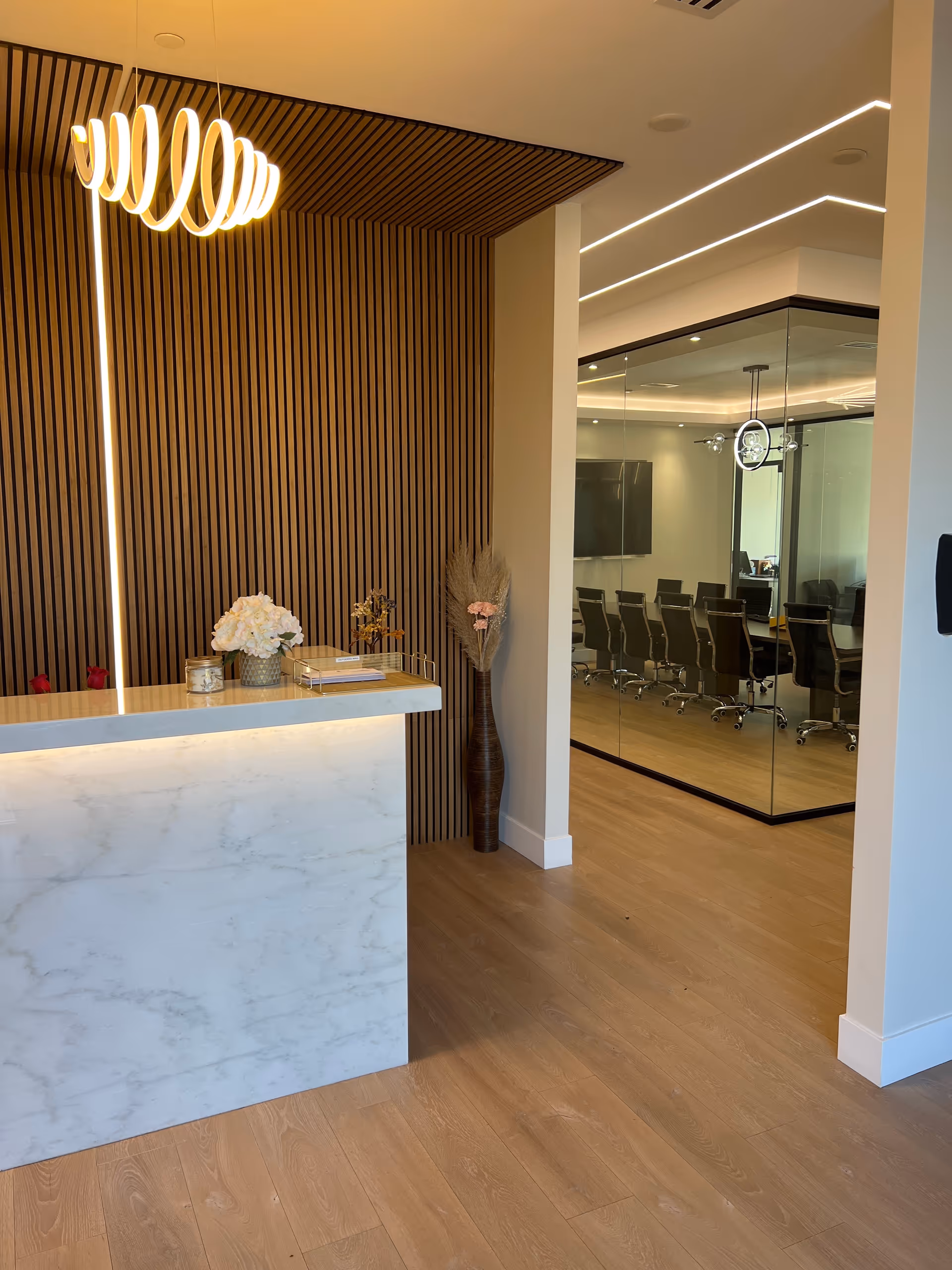 Modern reception area with marble front desk, wood slat wall, and glass-walled conference room.