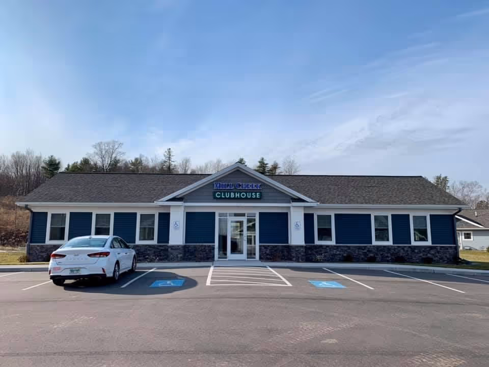 Front view of Mill Creek Clubhouse building with a parked car and accessible parking spaces.