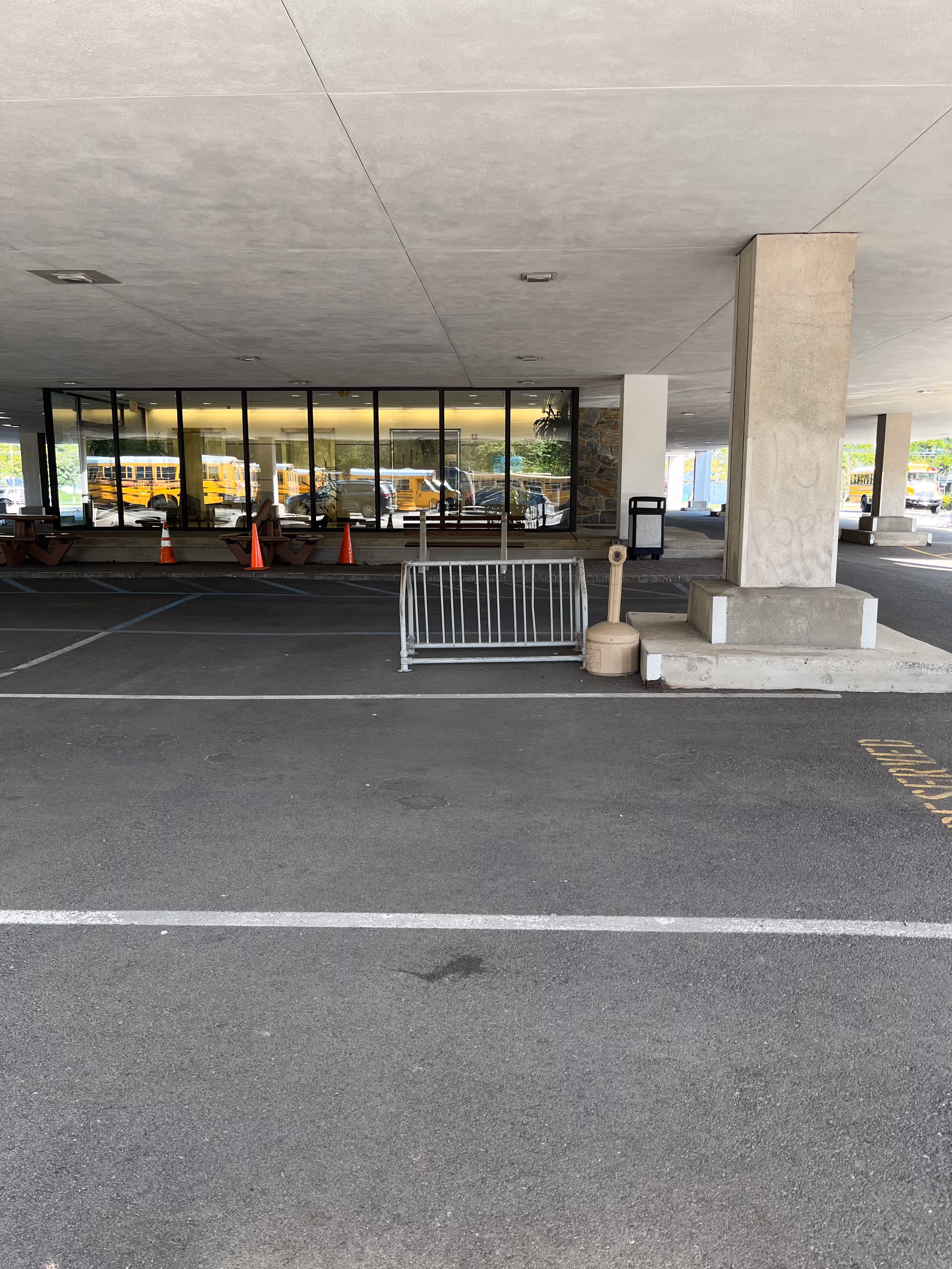 Covered parking area in front of a building with glass windows and cones.