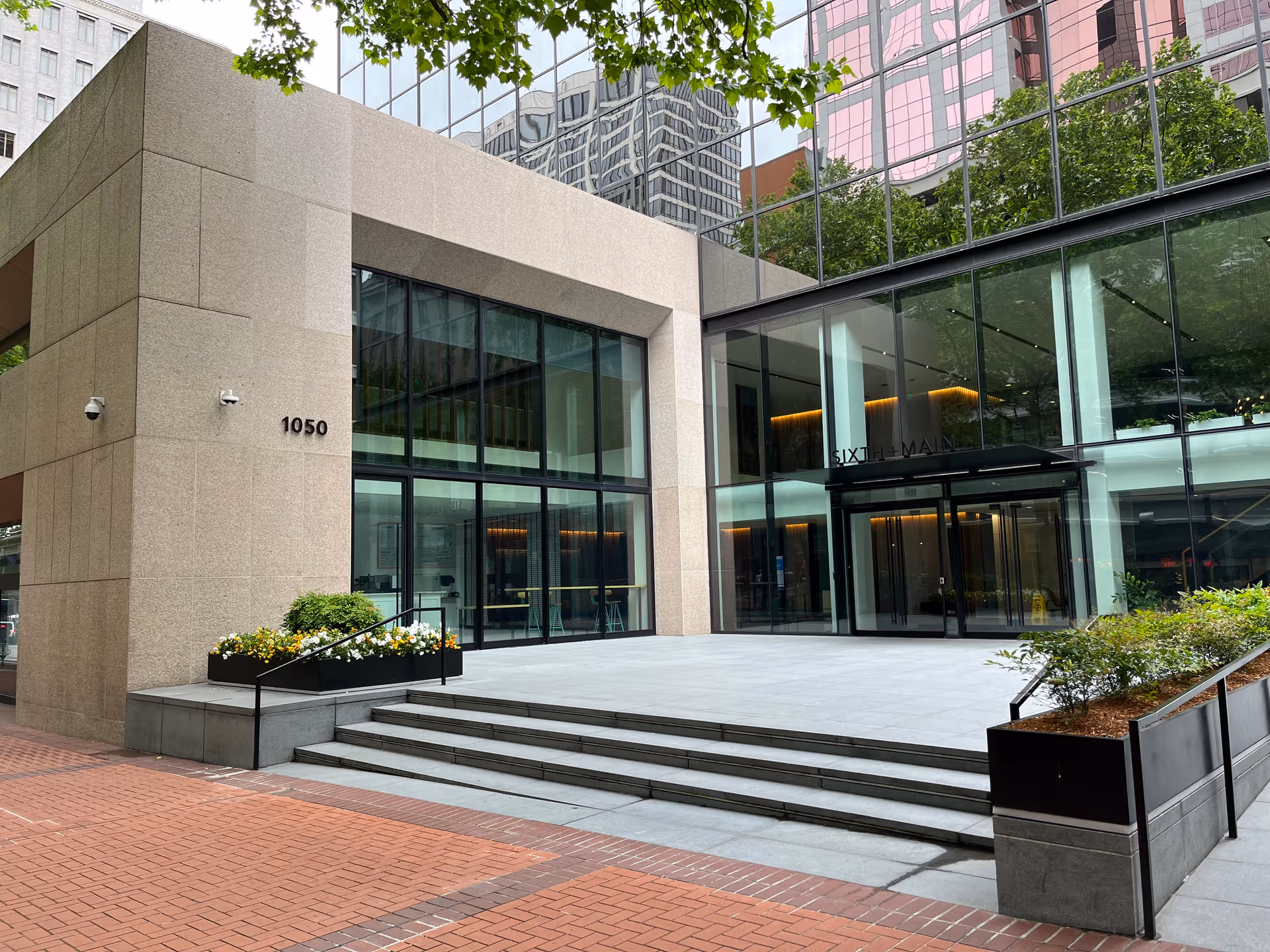 Modern glass-fronted building entrance with stairs and planters, urban exterior.