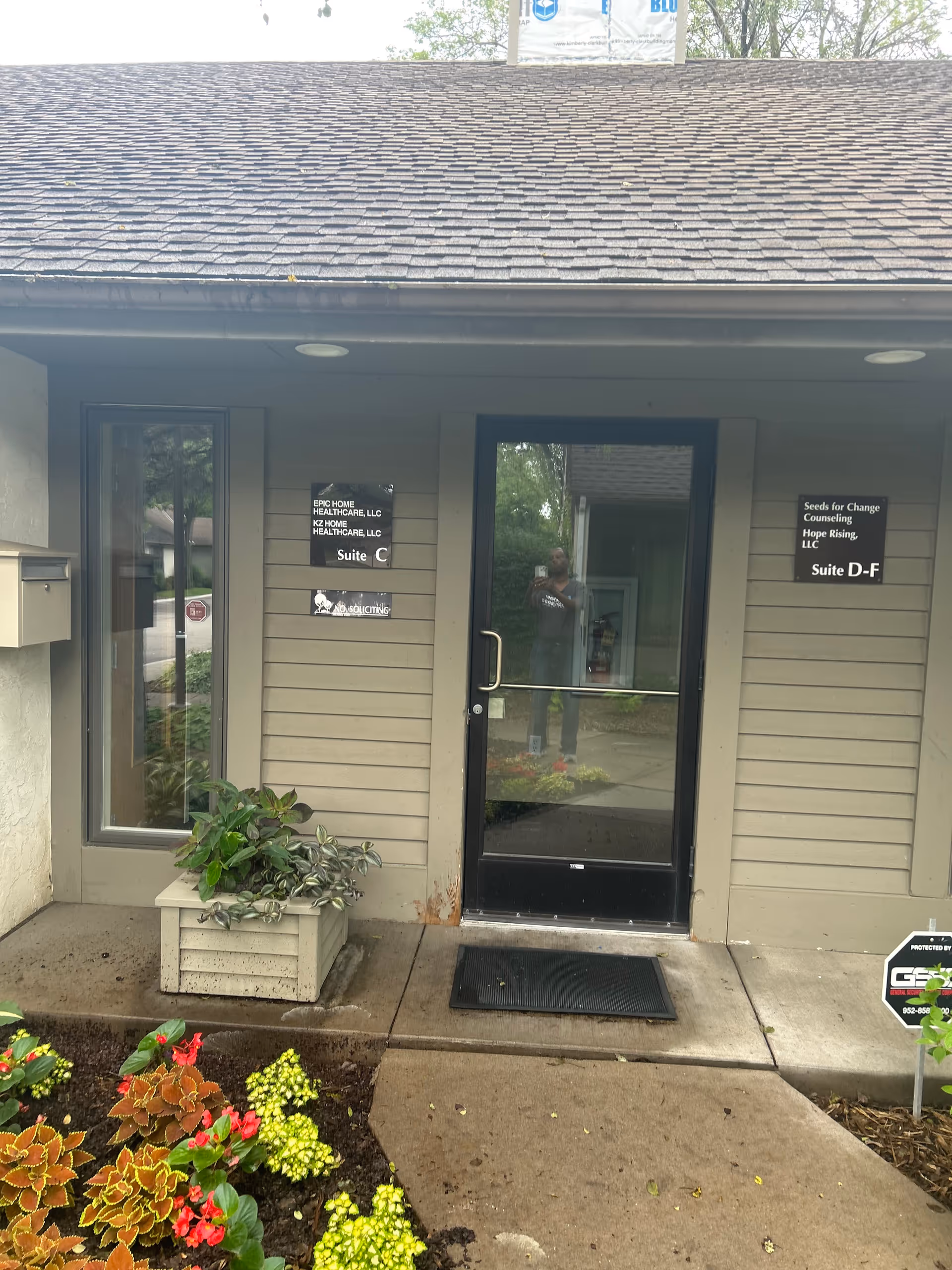 Exterior entrance to a senior care facility with signage, planters, and a glass door.