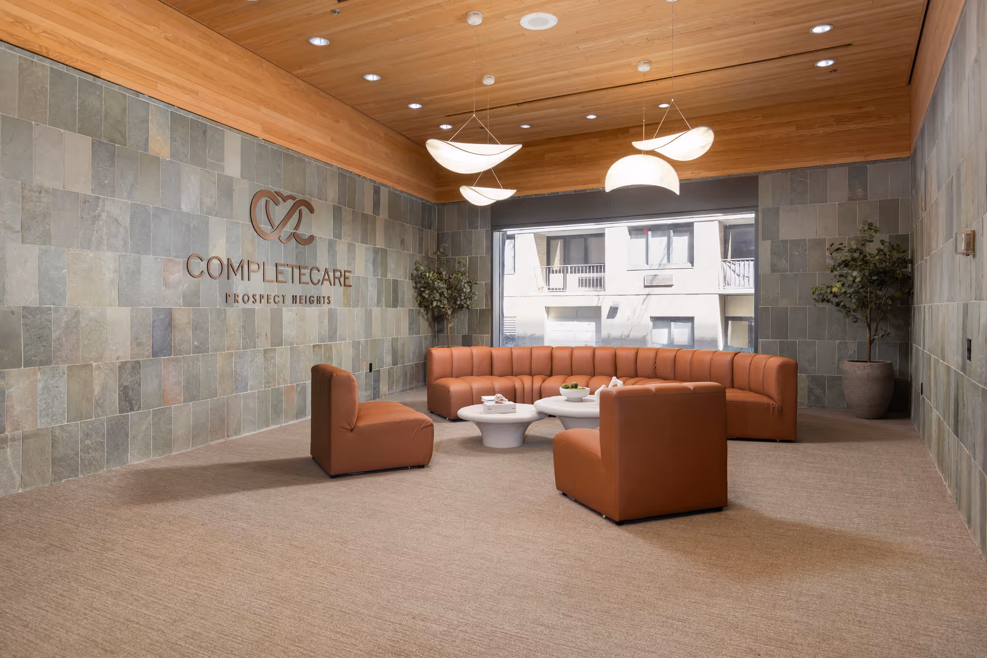 Interior lobby with orange curved seating, white coffee tables, tile walls, and potted plants.