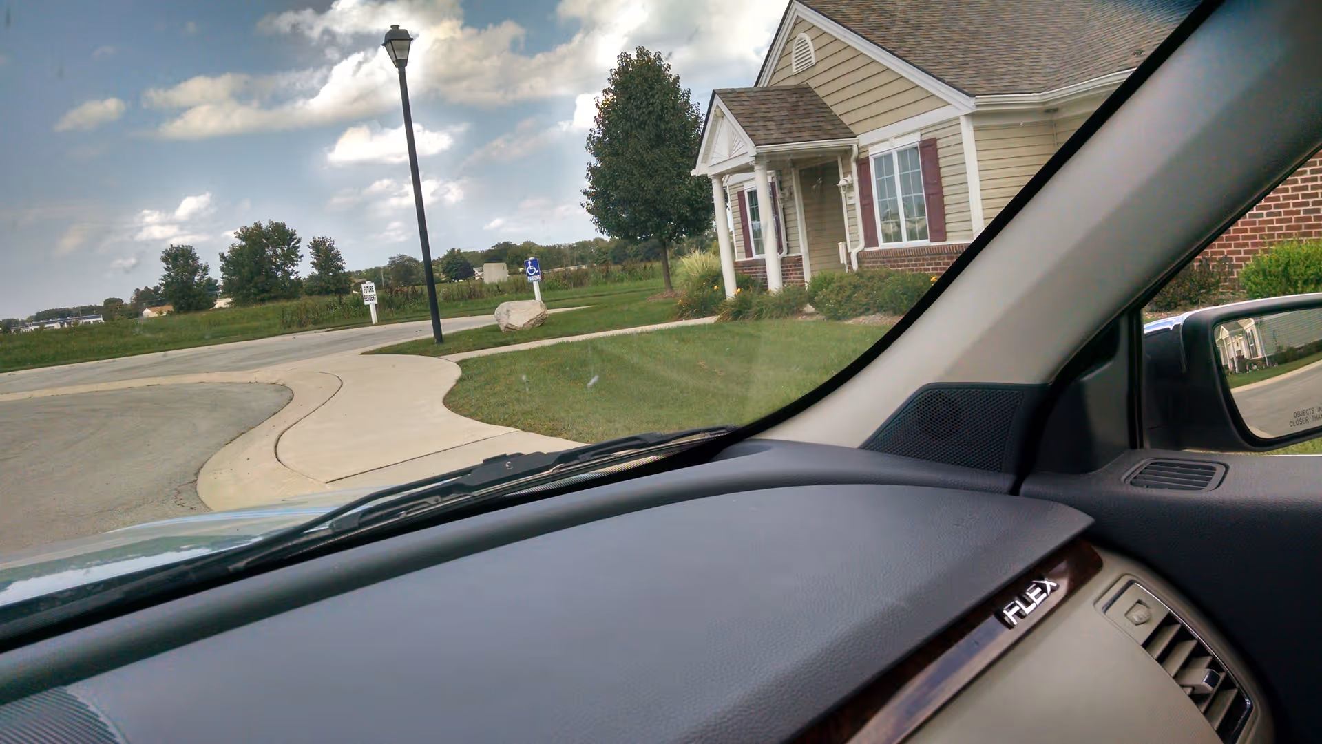 View from inside a car showing the front of a senior living facility and curved driveway.
