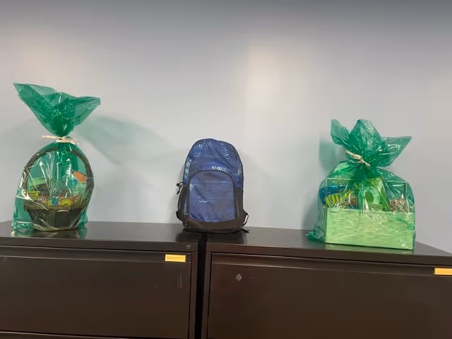 Blue backpack between two green gift baskets atop dark cabinets against a light wall.