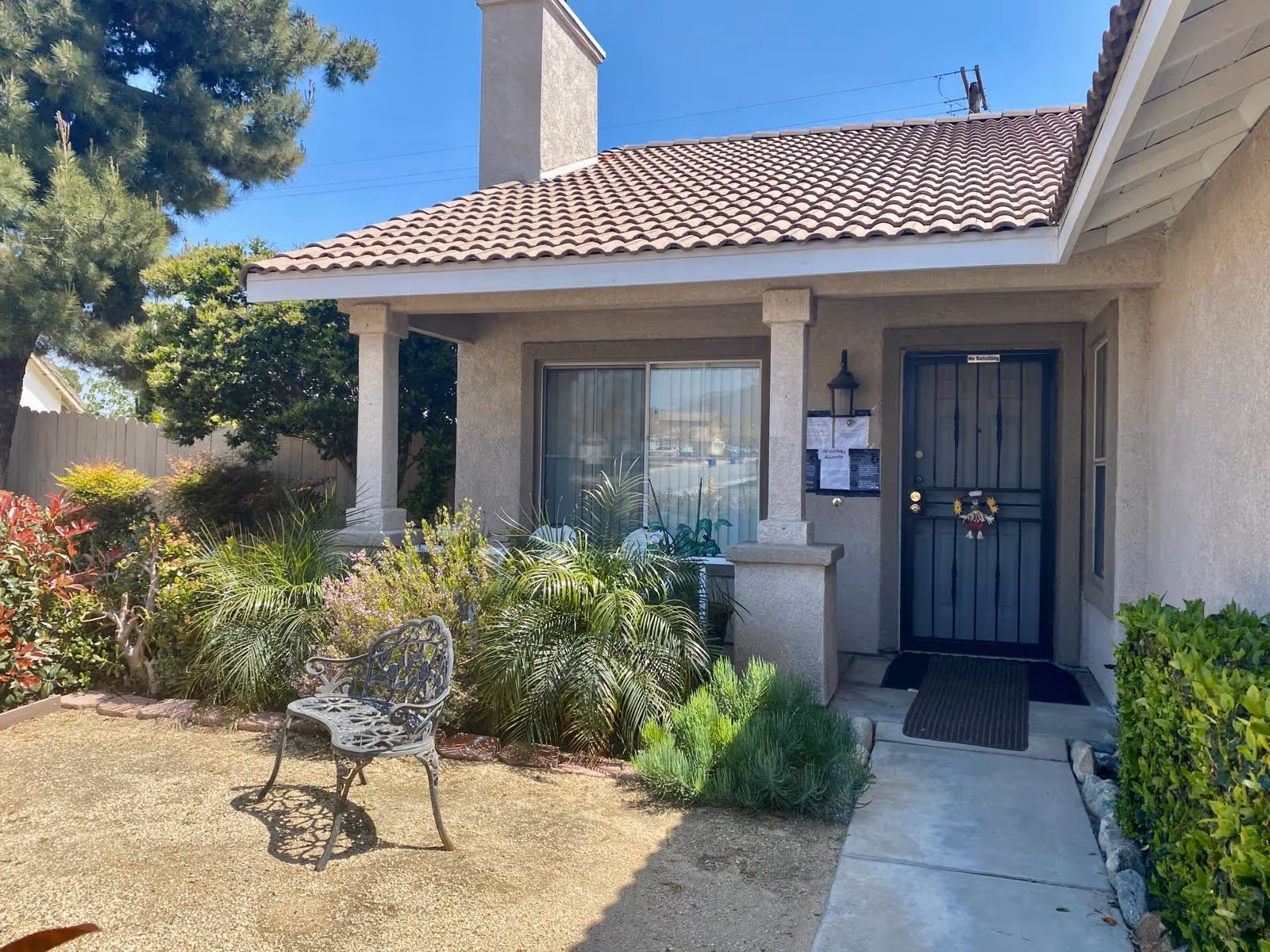 Front exterior of a senior living facility with a blue door, porch, and landscaping.