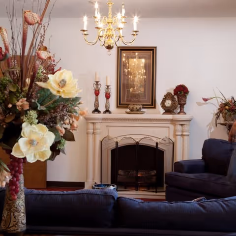 Living room with chandelier, fireplace mantel, floral arrangement, and blue sofas.