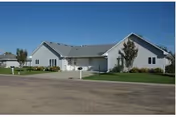 Single-story senior living facility front exterior with driveway, mailbox, and manicured lawn.