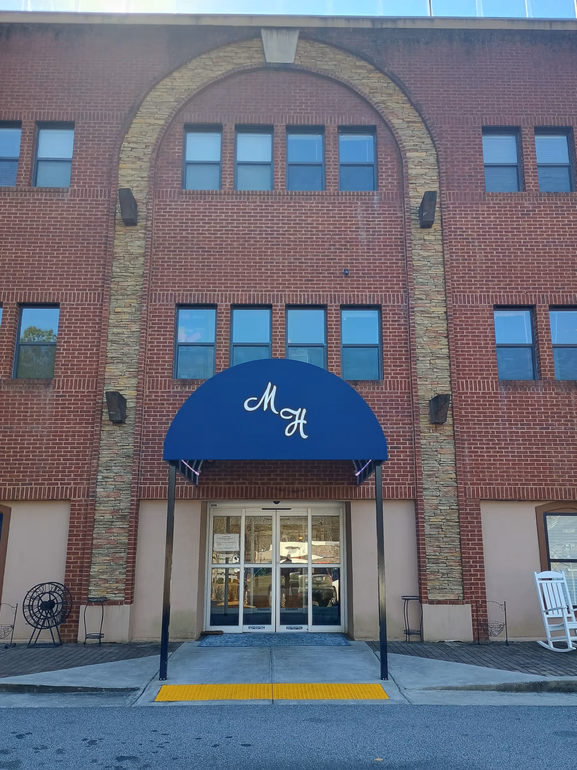 Brick building front with blue curved awning over glass doors at Monarch House in Newnan, Georgia.