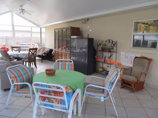Covered outdoor patio with colorful chairs around a green table and a TV
