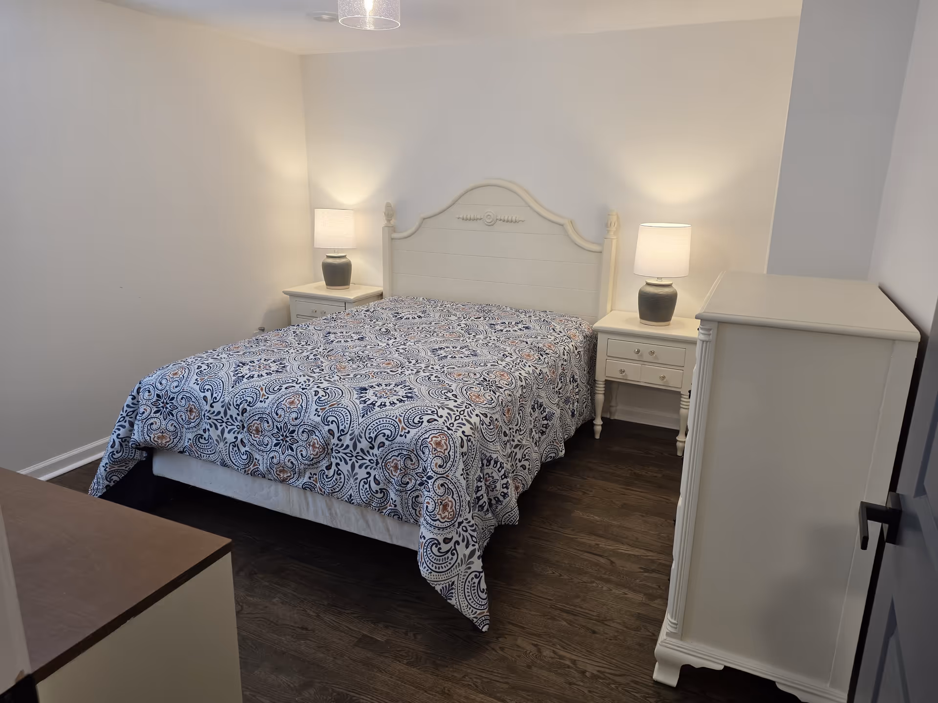 A neatly furnished bedroom with a bed, two nightstands, lamps, and a dresser.