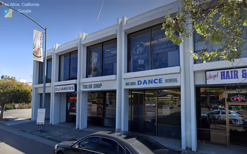 Exterior view of a storefront building with signs for cleaners, tailor shop, and dance school.