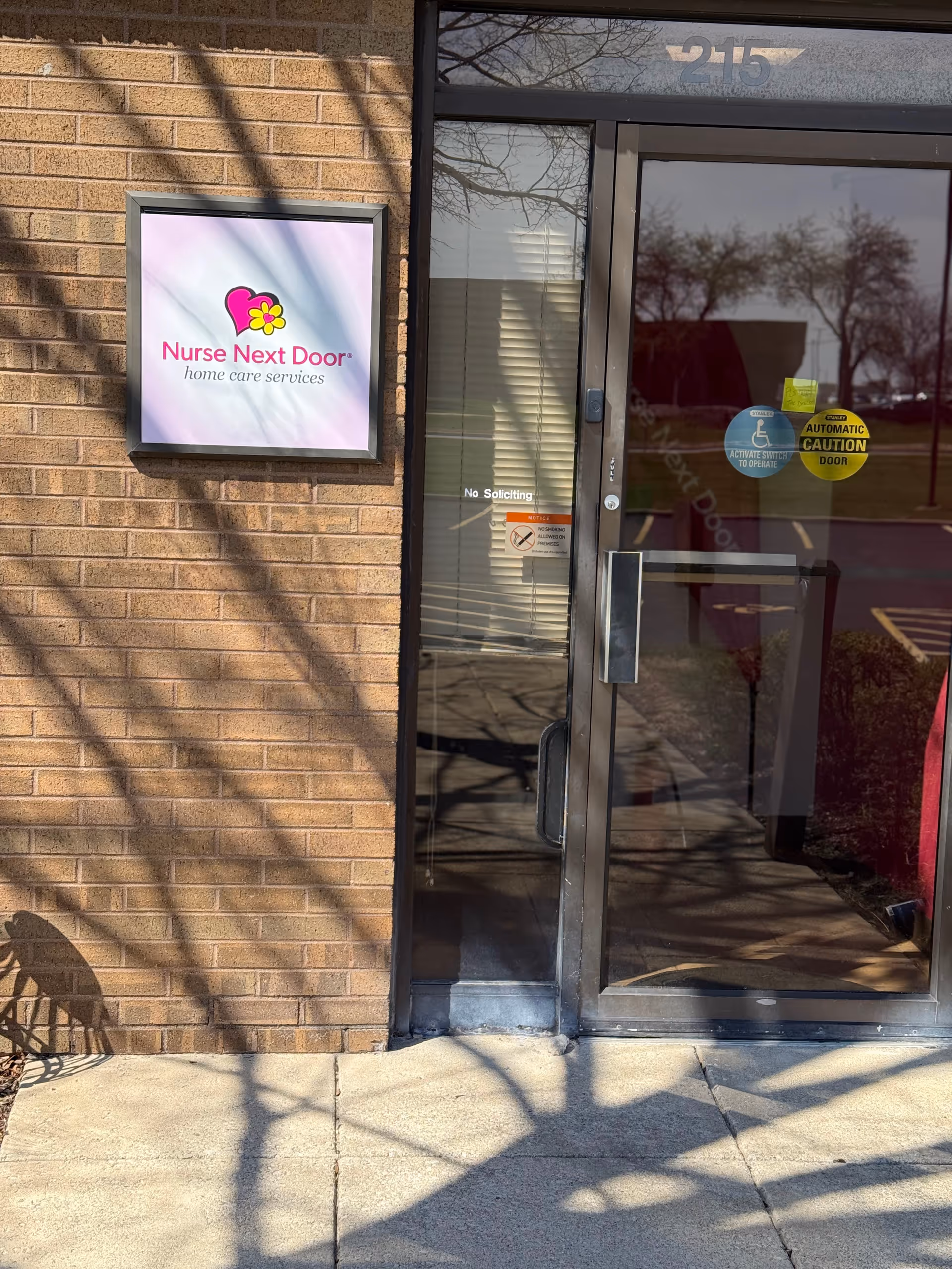 Brick exterior entrance with Nurse Next Door sign beside glass door and No Soliciting sticker.
