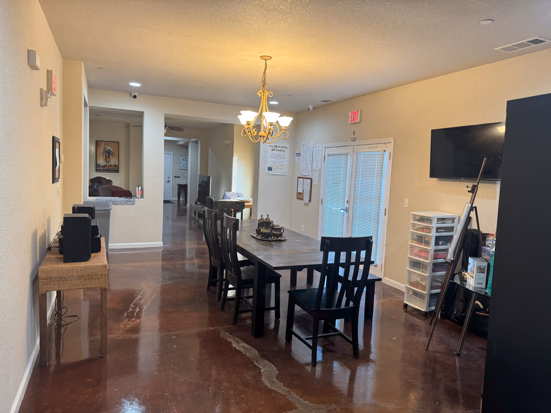 A long dining table with chairs occupies a bright communal room in a senior living facility.