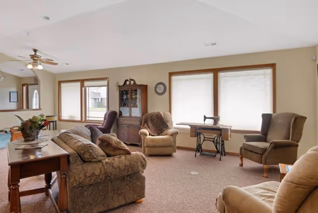 Cozy living room with sofas, chairs, and large windows in a senior facility's common area.