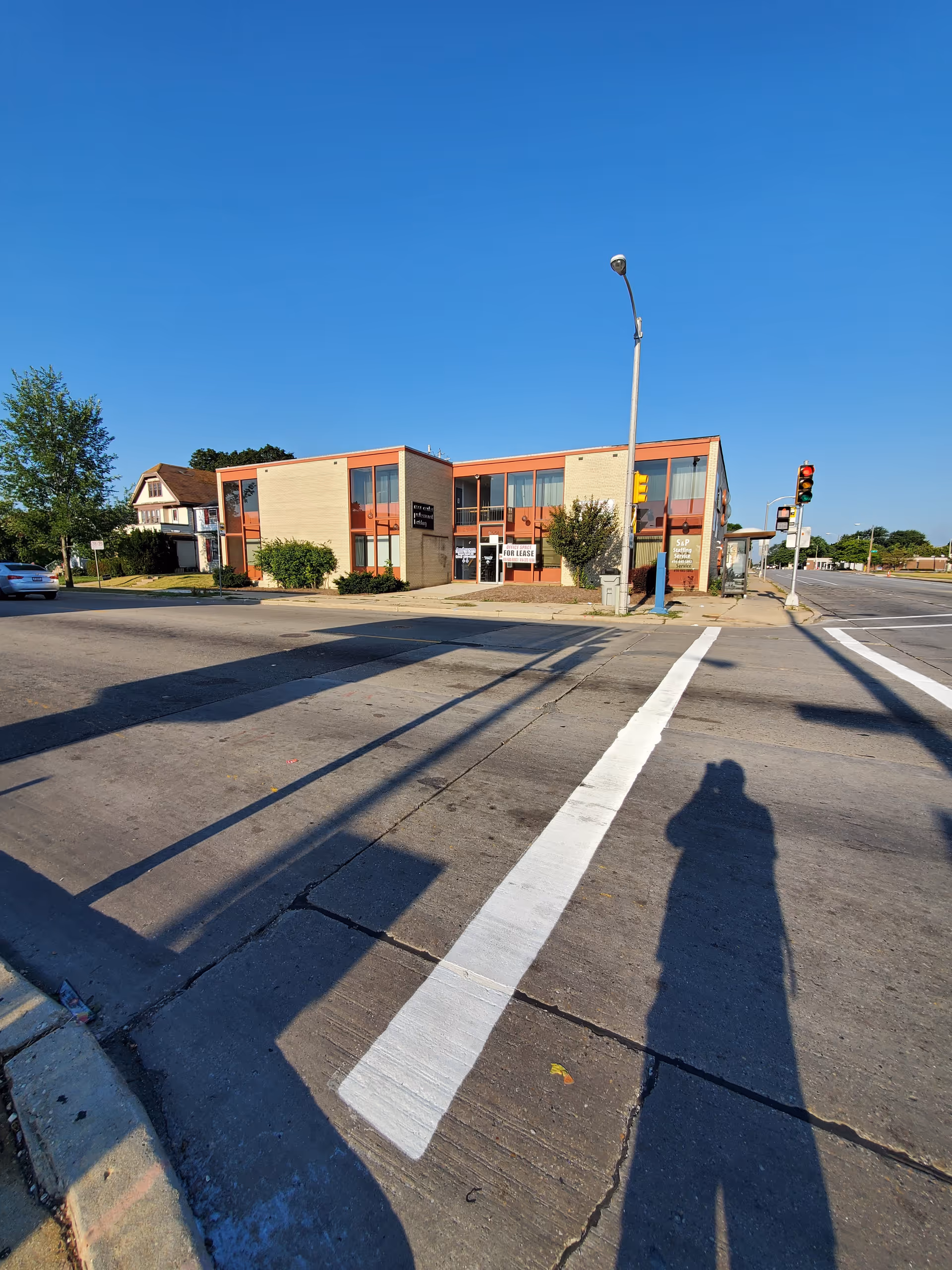 Two-story brick building on a street corner with a crosswalk and long shadows.