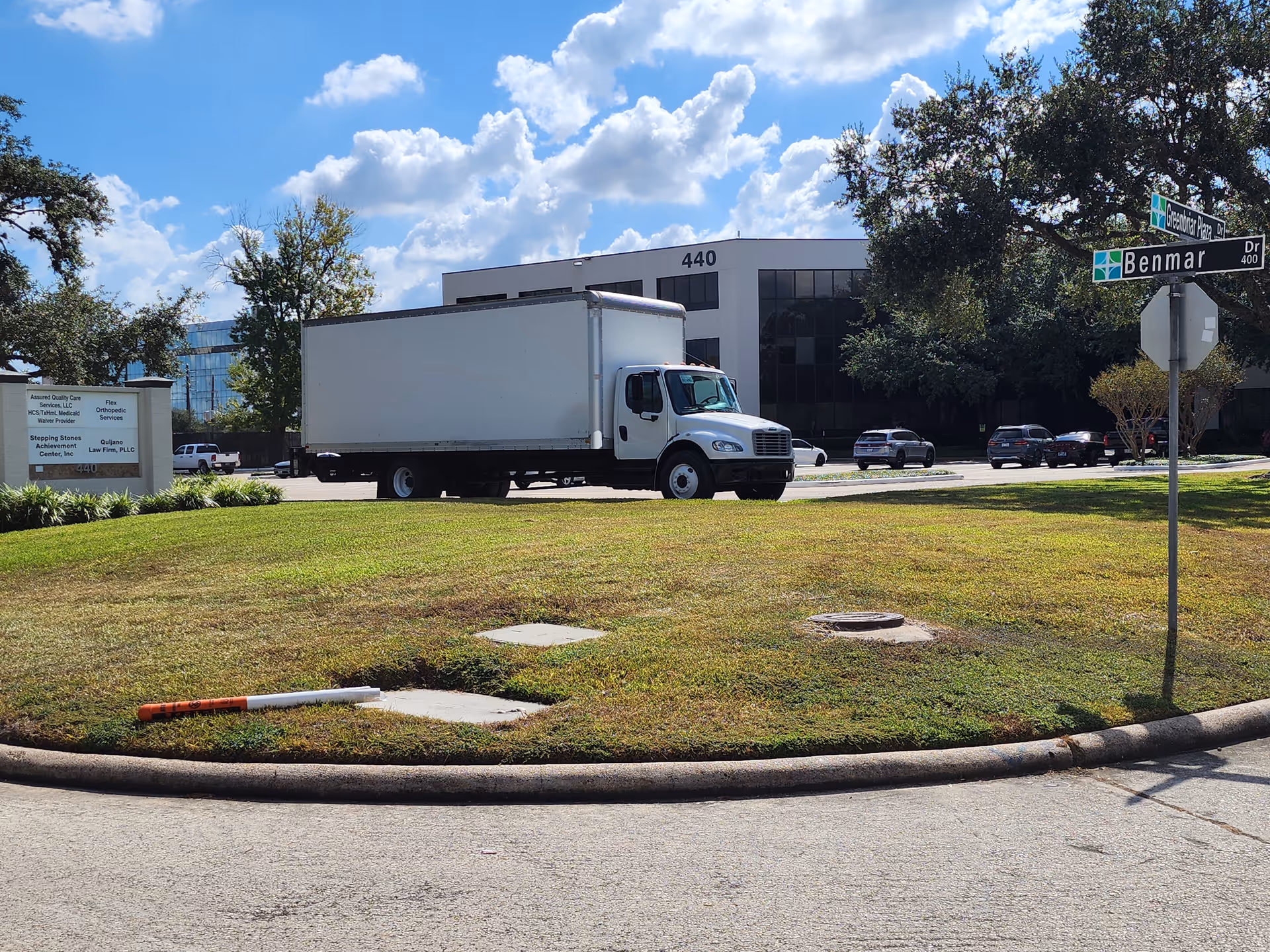 Exterior view of a corporate office campus with a white box truck near a grassy roundabout.