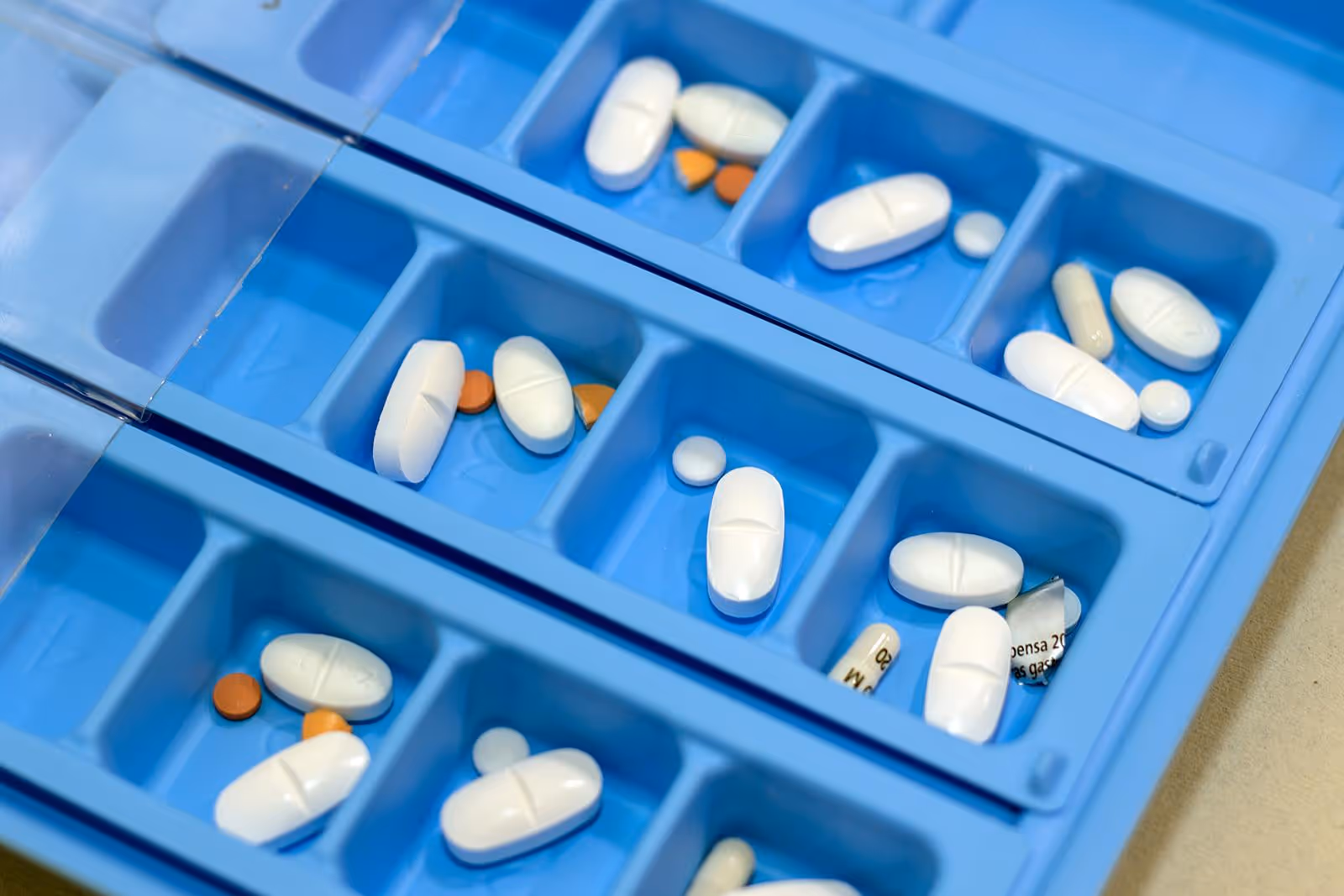 Blue medication organizer with white and orange pills arranged in compartments.