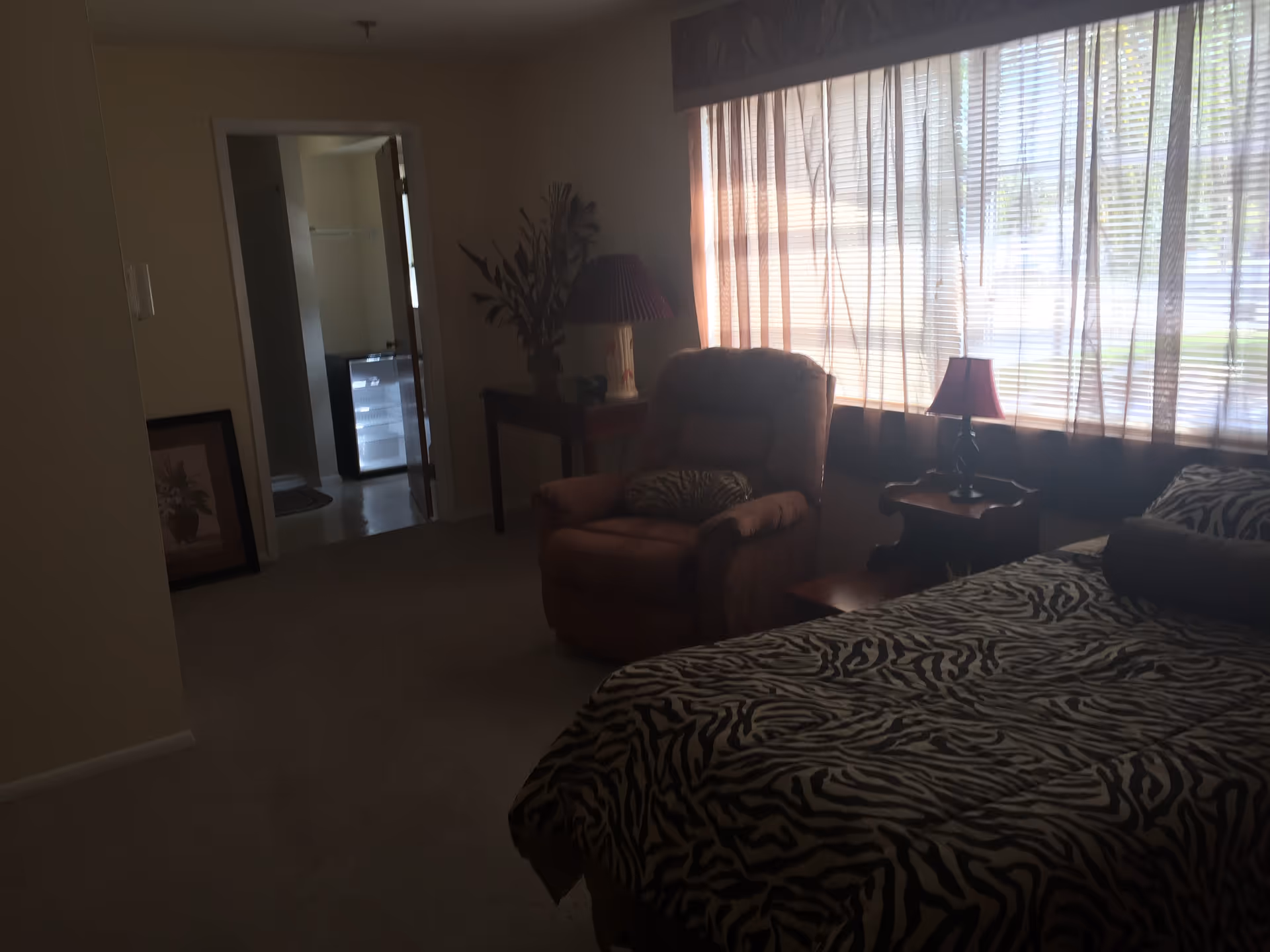 Cozy bedroom featuring zebra-patterned bedding, an armchair, lamps, and a large window with blinds.