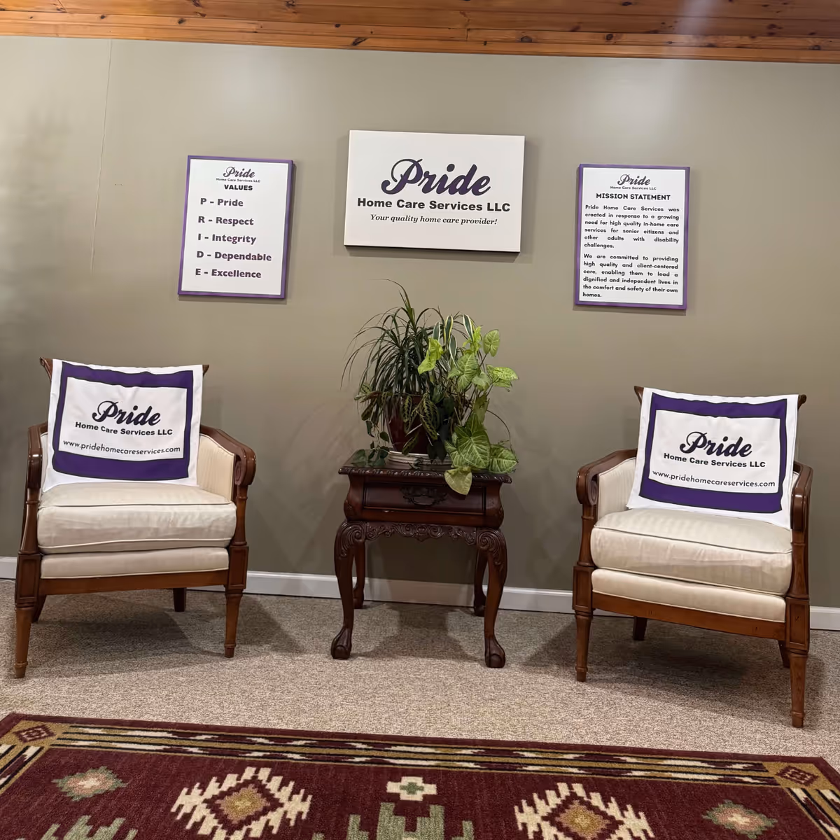 Two wooden chairs with Pride pillows flank a plant on a carved table in a lobby.