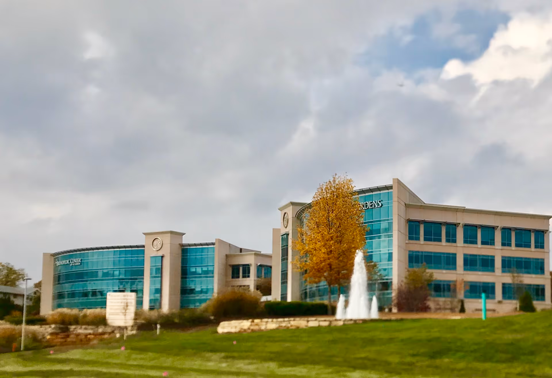 Exterior view of Delmar Gardens Private Services building with a central fountain and blue glass facade.