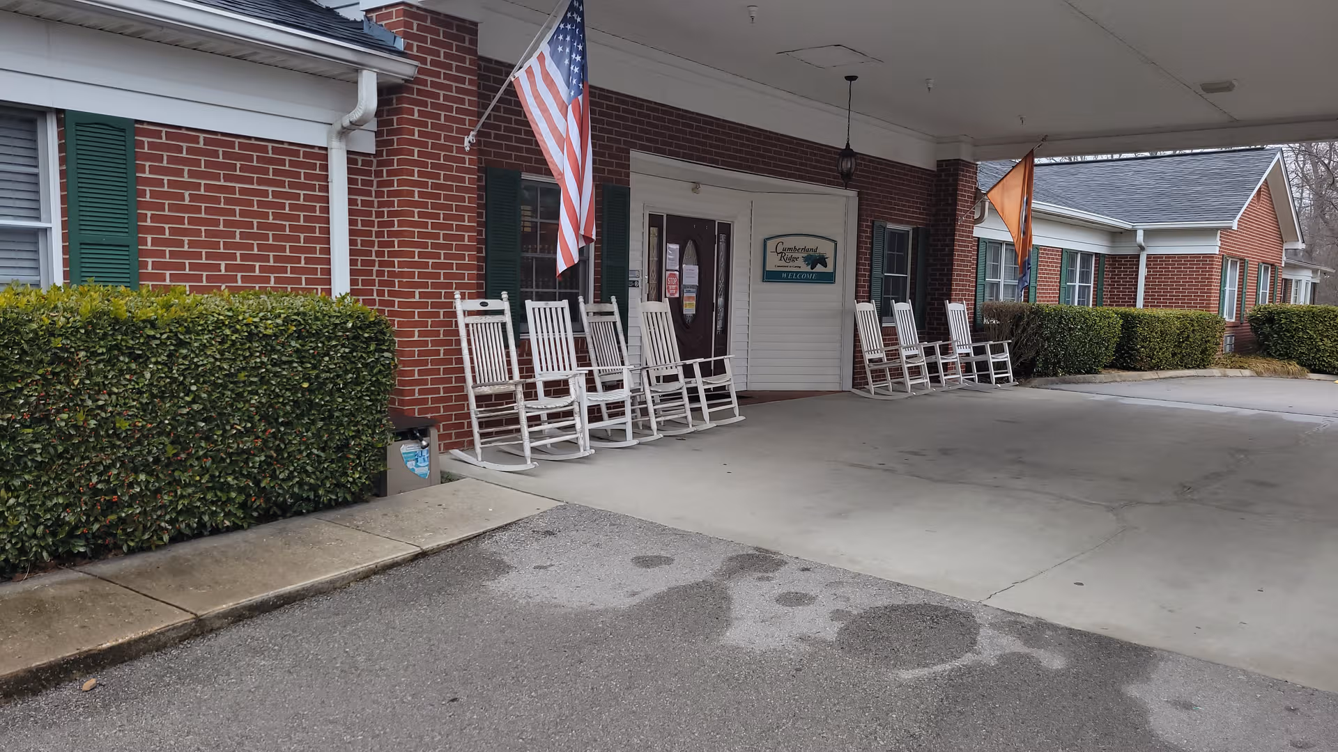Exterior view of Cumberland Ridge Assisted with a covered entry, rocking chairs, and flags.