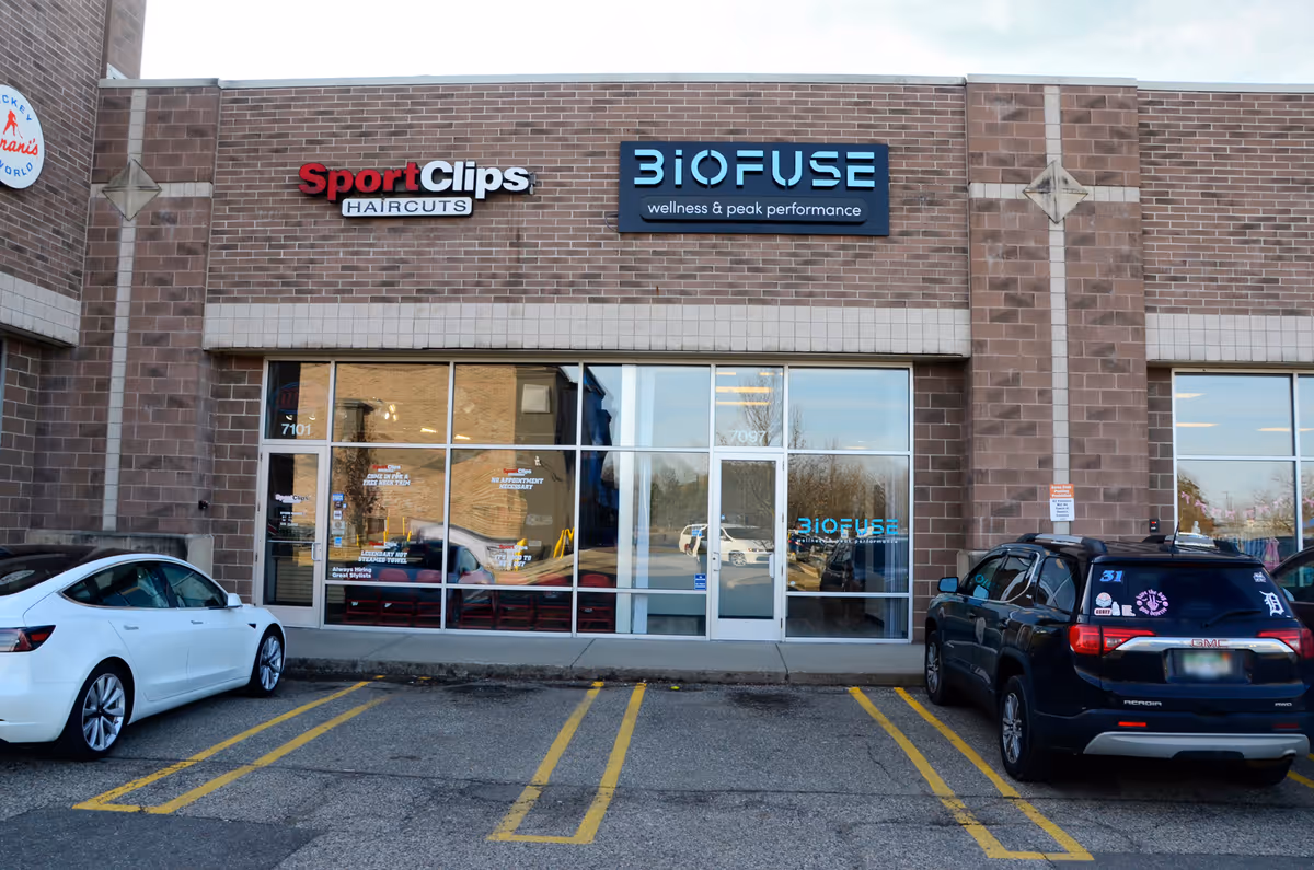 Exterior storefront of BioFUSE with Sport Clips in brick shopping plaza, cars parked.