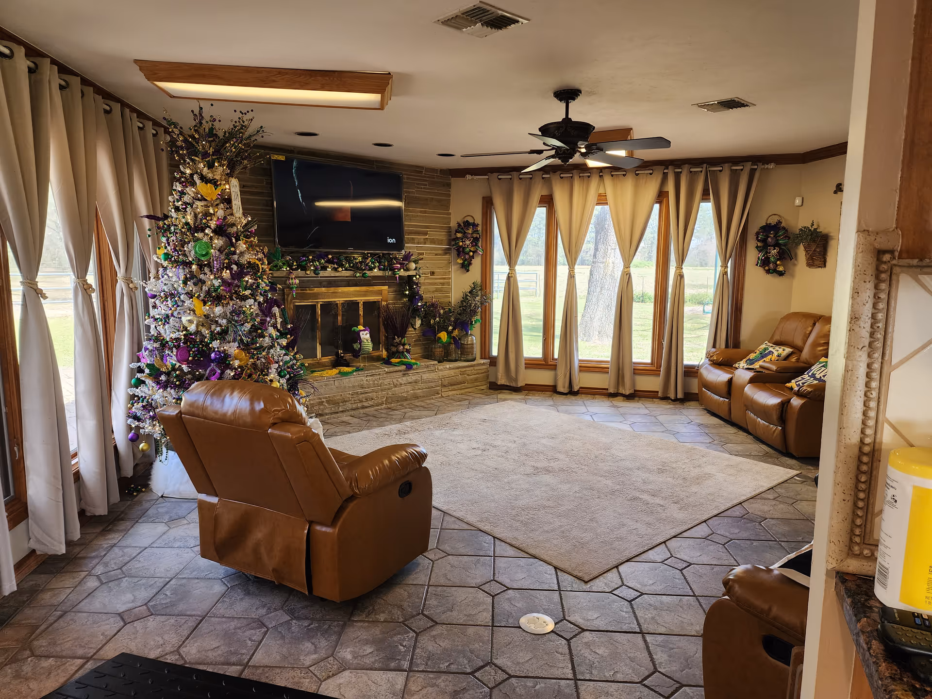Cozy living room with a Christmas tree, brown recliners, fireplace, and large windows.