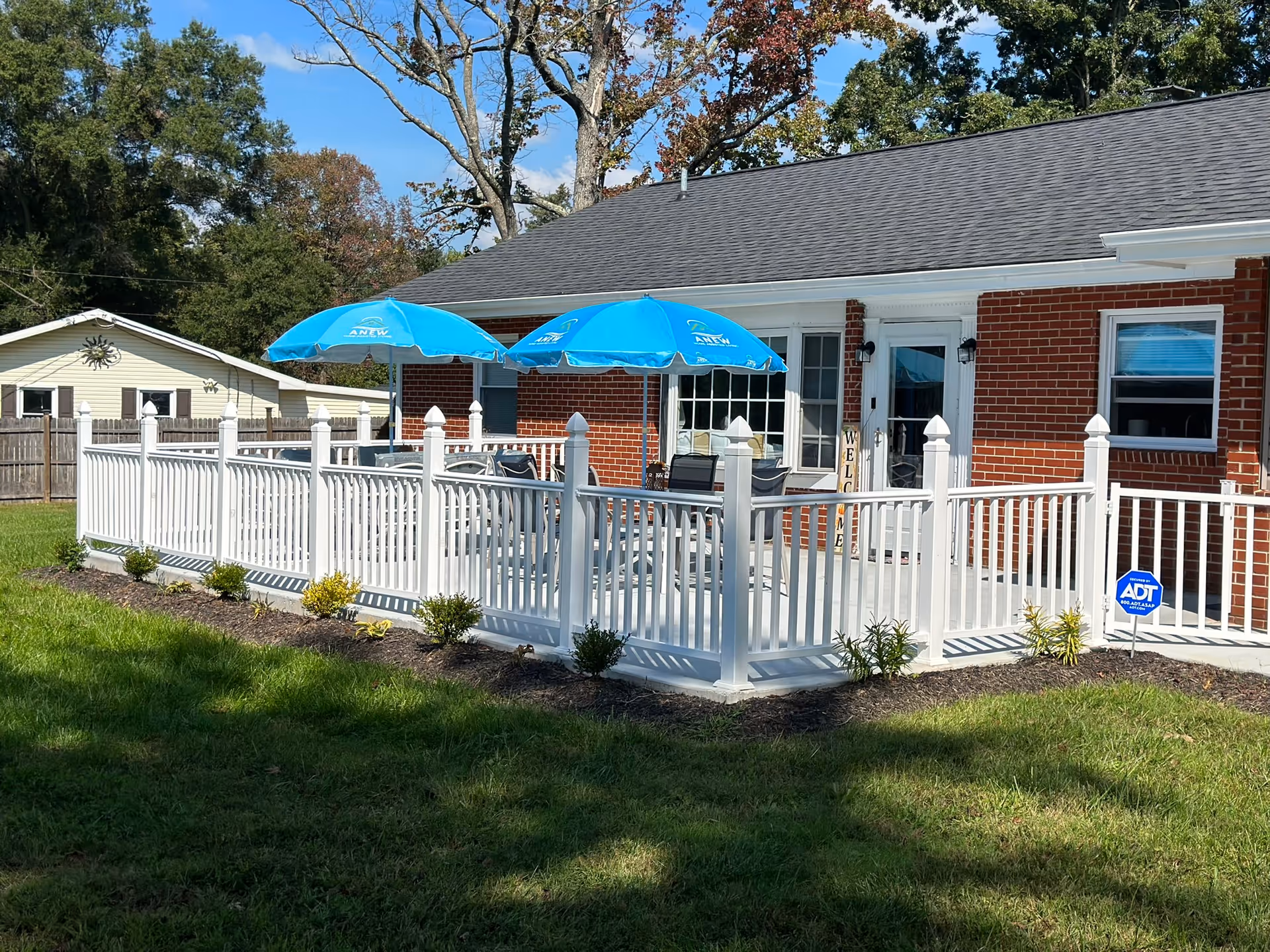 Brick senior living home with white fenced outdoor deck and blue patio umbrellas.