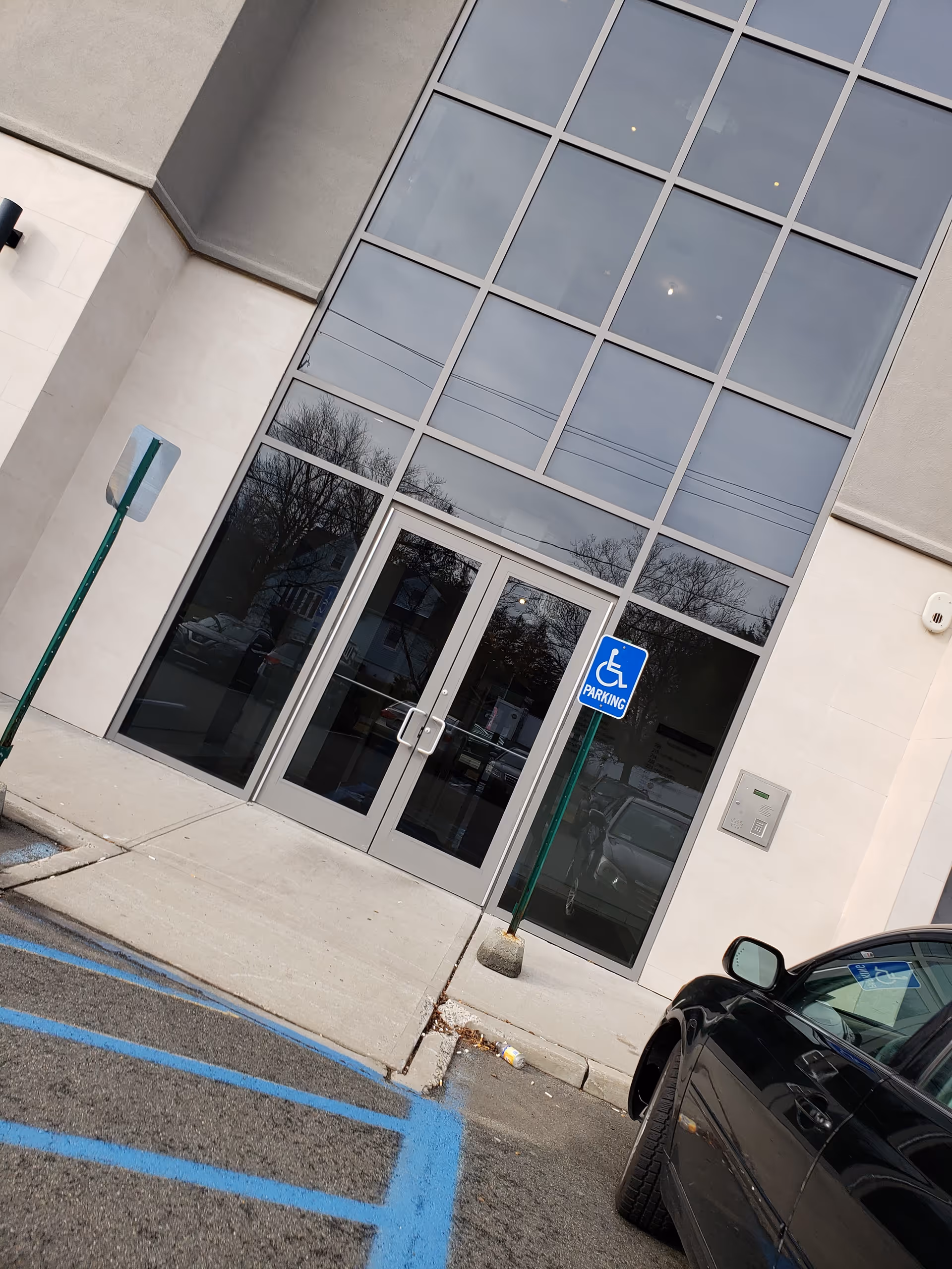 Modern building entrance with tall glass windows and a handicap parking sign.