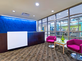 Modern reception area with blue wall, magenta chairs, and glass partition.