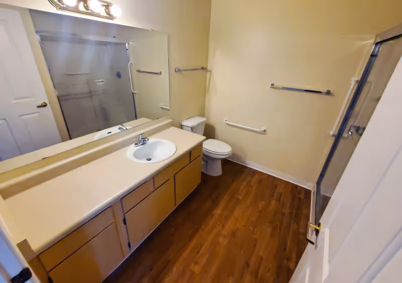 Bathroom with long beige vanity, mirror, toilet, and glass-enclosed shower.
