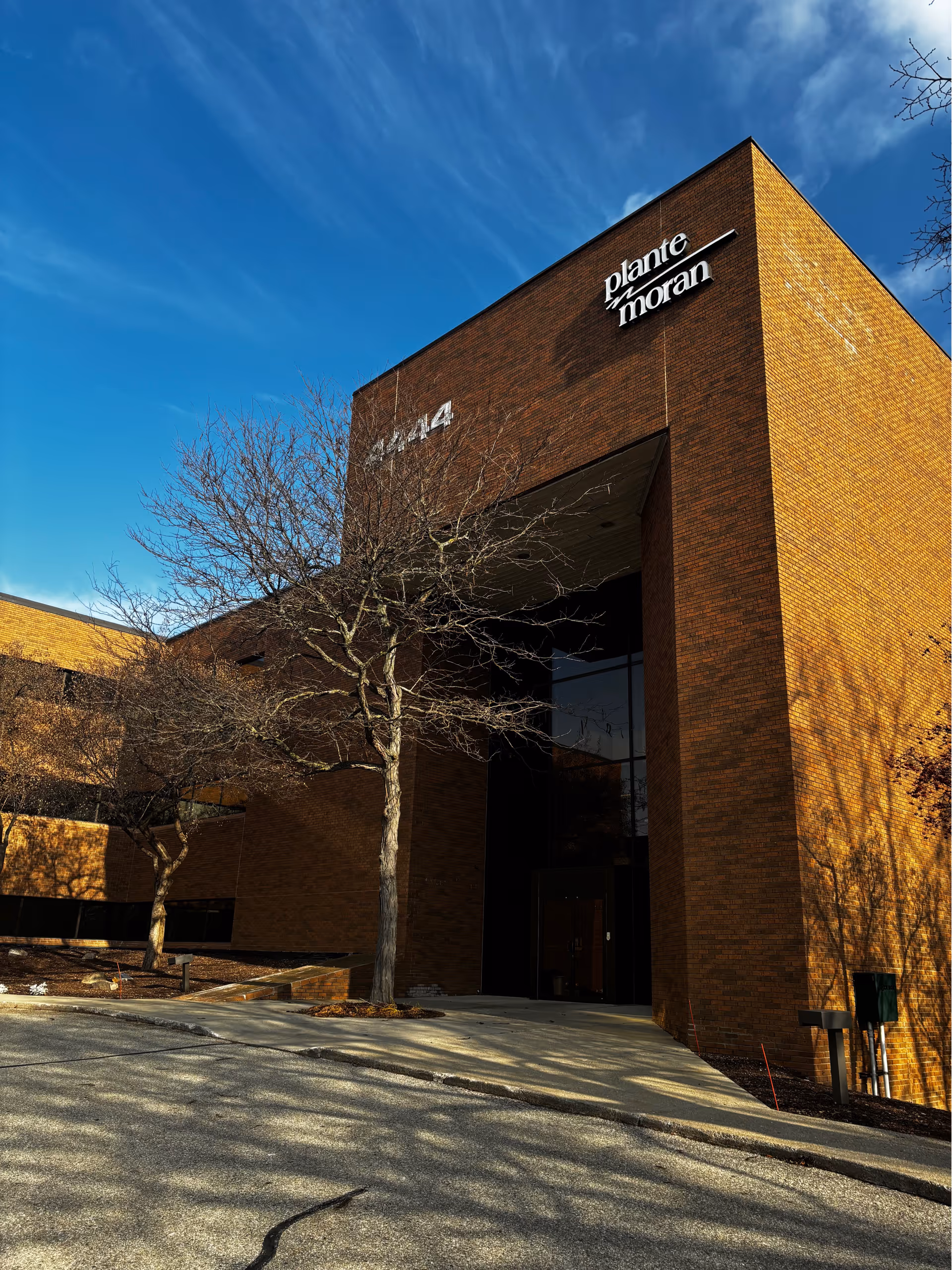 Brick building exterior with a tall entrance, leafless trees, and a blue sky.