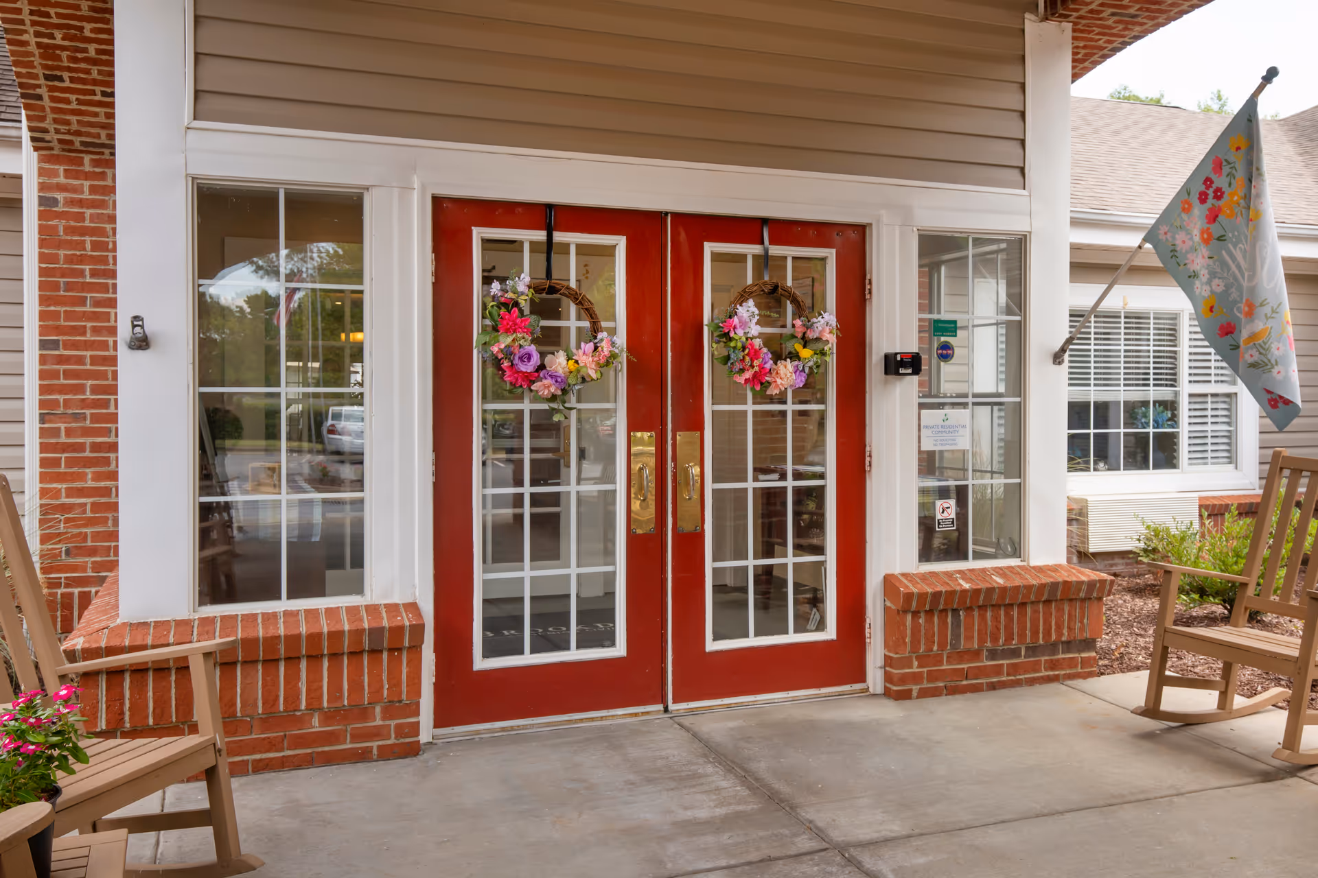 Red double doors with wreaths, brick planters, and outdoor seating at the facility entrance.