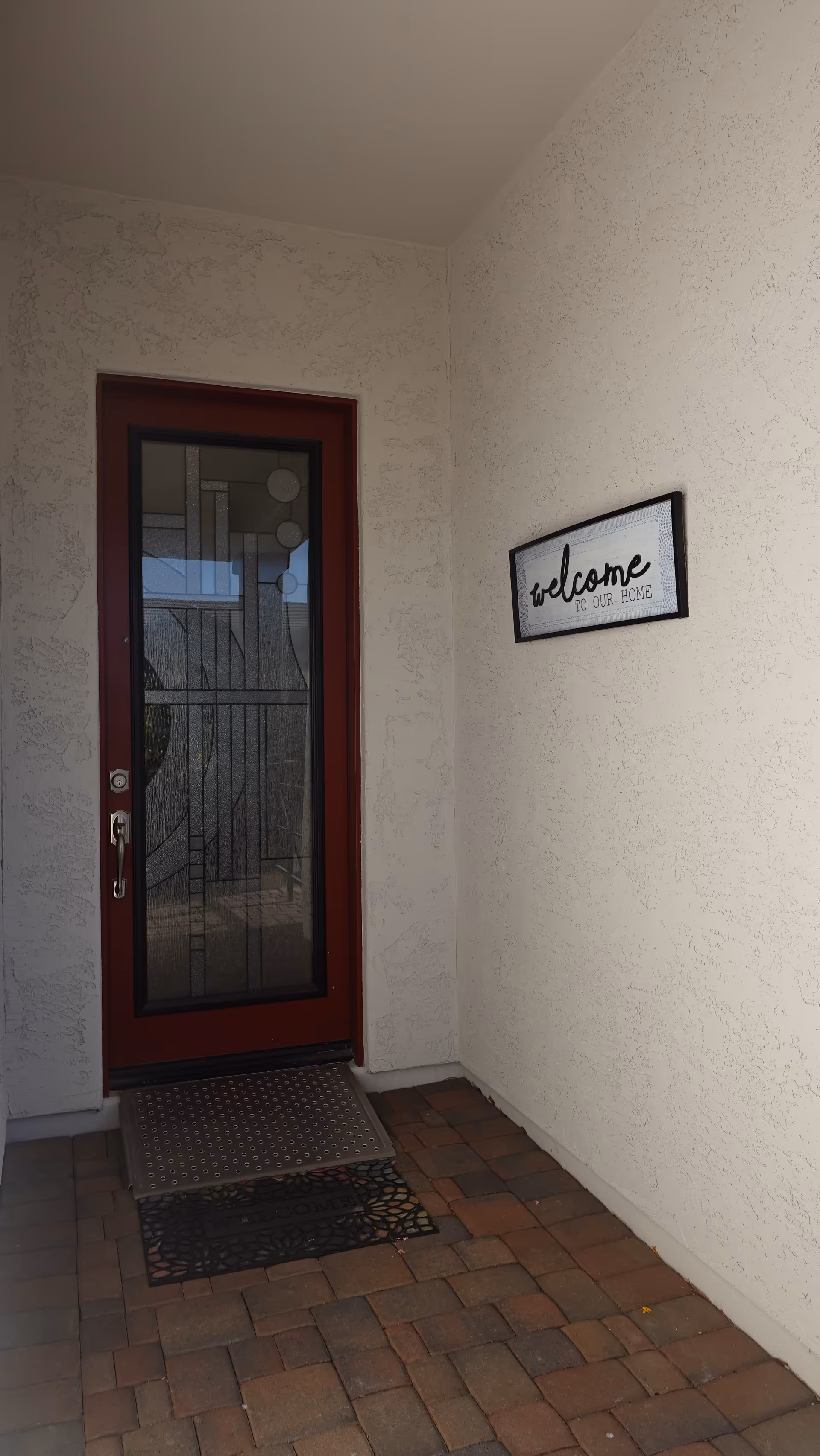 Red-framed glass entry door with a welcome sign on textured beige exterior walls.