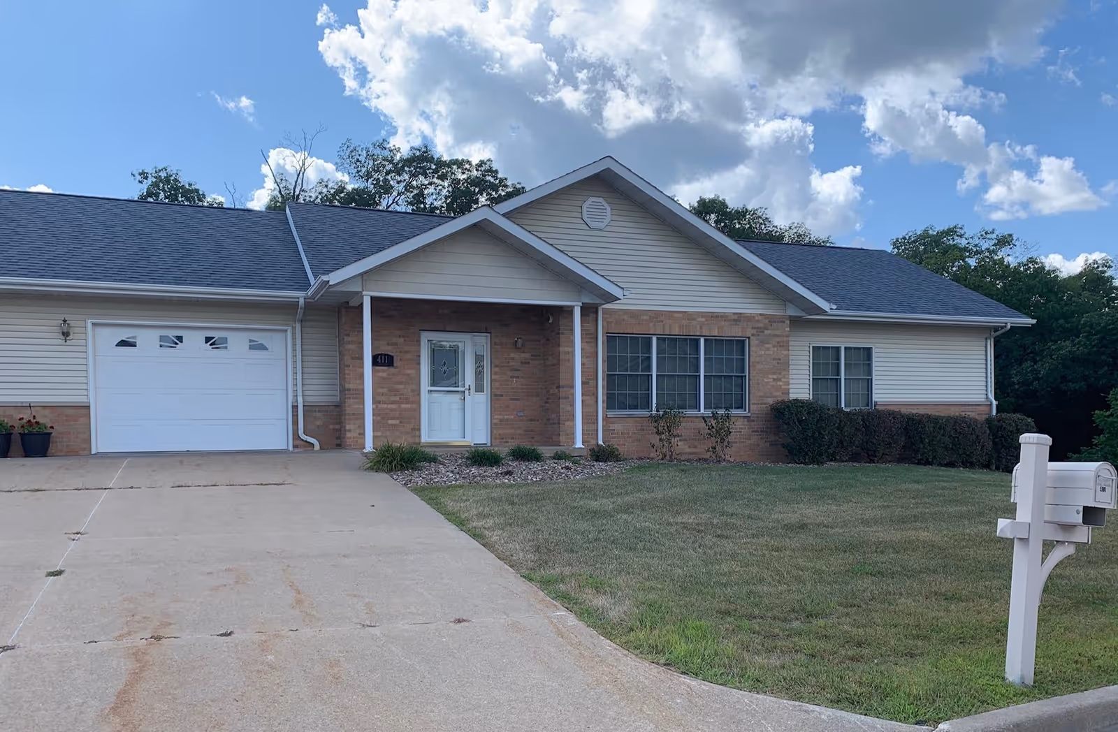 Single-story senior living facility exterior with driveway, front entrance, garage, and landscaped lawn.