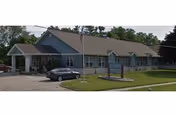 Blue, single-story senior living facility exterior with parked car and manicured lawn.