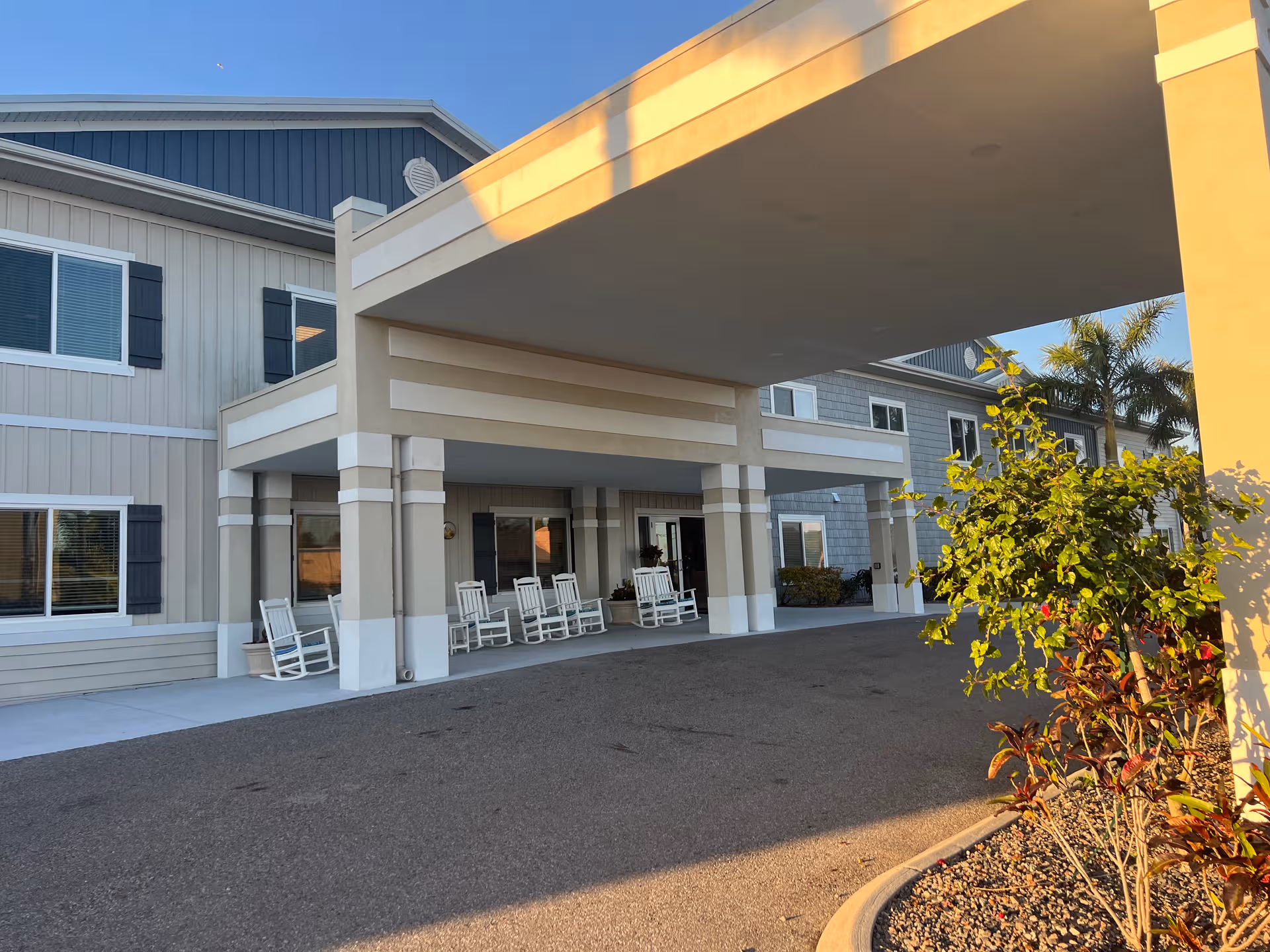 Front entrance of Villas of Holly Brook senior living with a covered drop-off and rocking chairs.