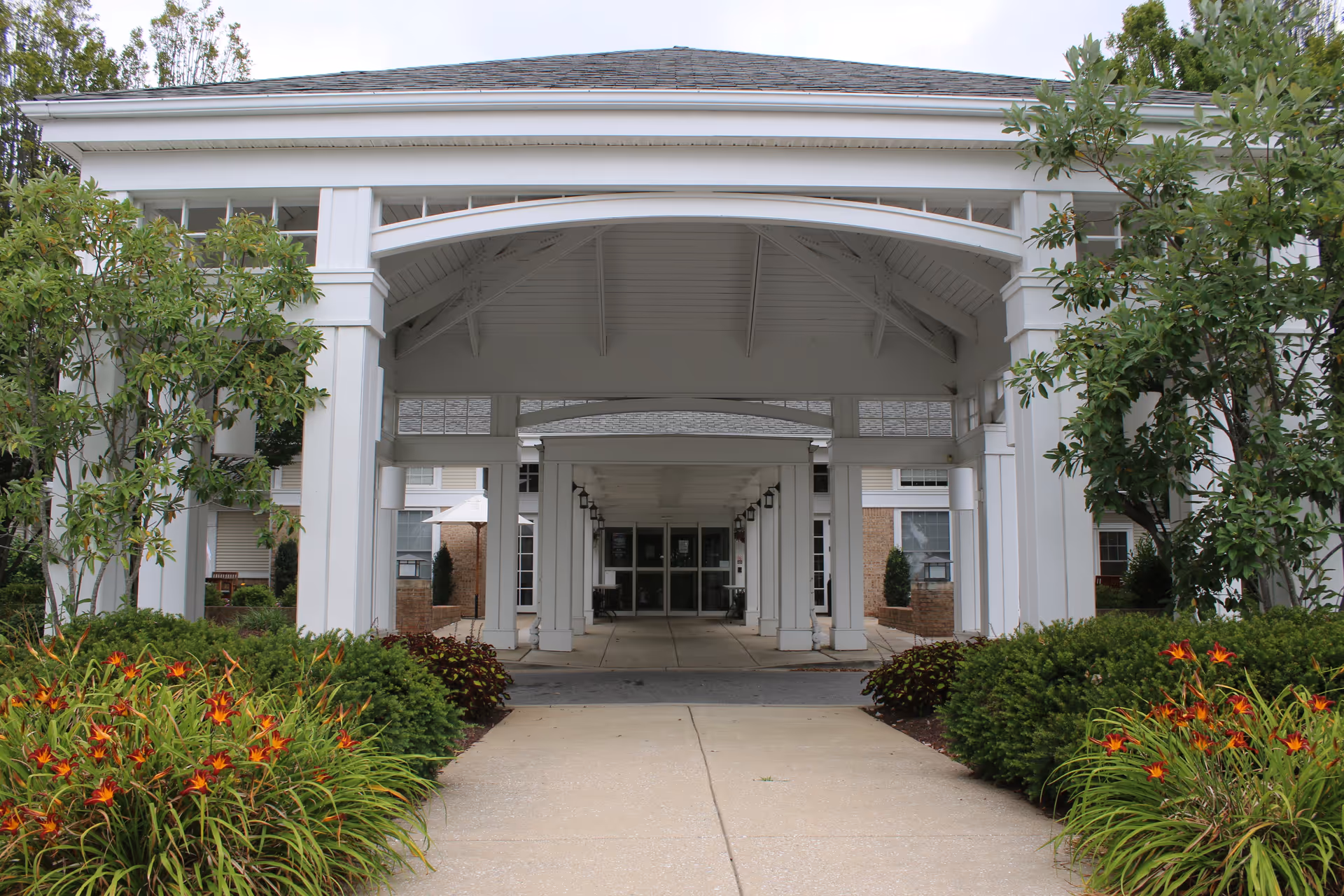 White entrance portico with columns leads into Integrace Copper Ridge Assisted Living, flanked by landscaped shrubs.