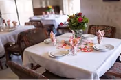 An interior dining room with tables set for meals, floral centerpieces, and folded napkins.