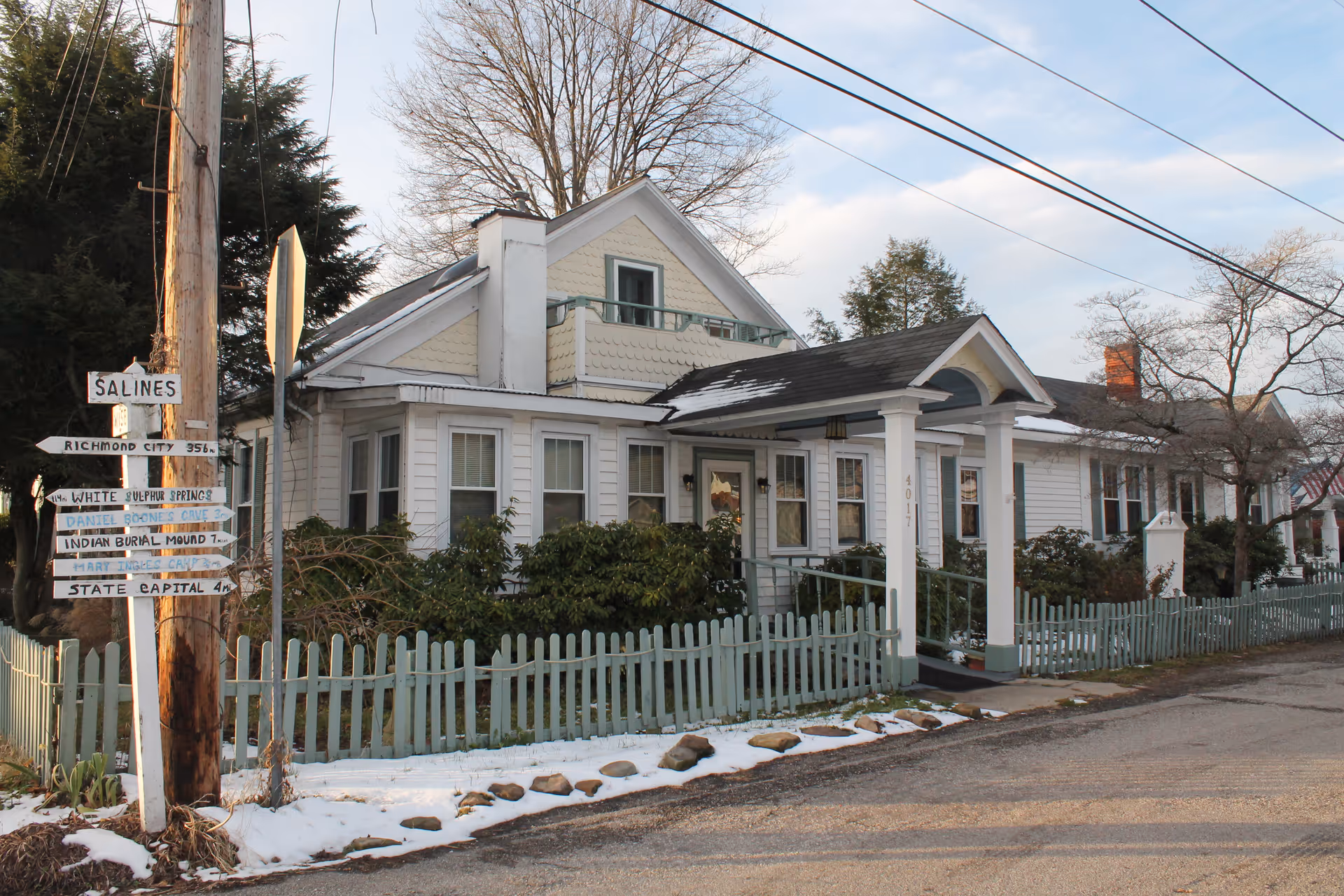 A small white house-like senior living facility with a pale blue fence along a snowy street