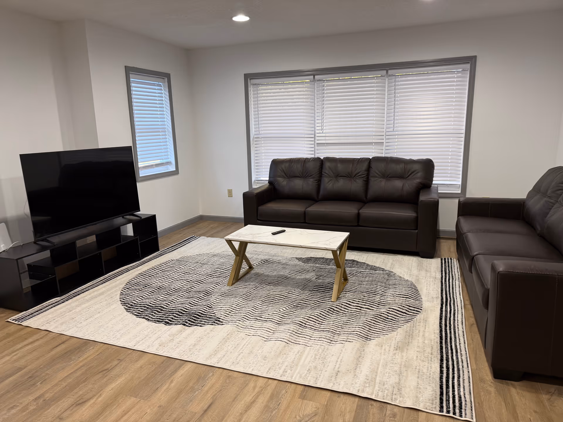 Living room with dark brown sofas, coffee table, TV, and large window blinds.