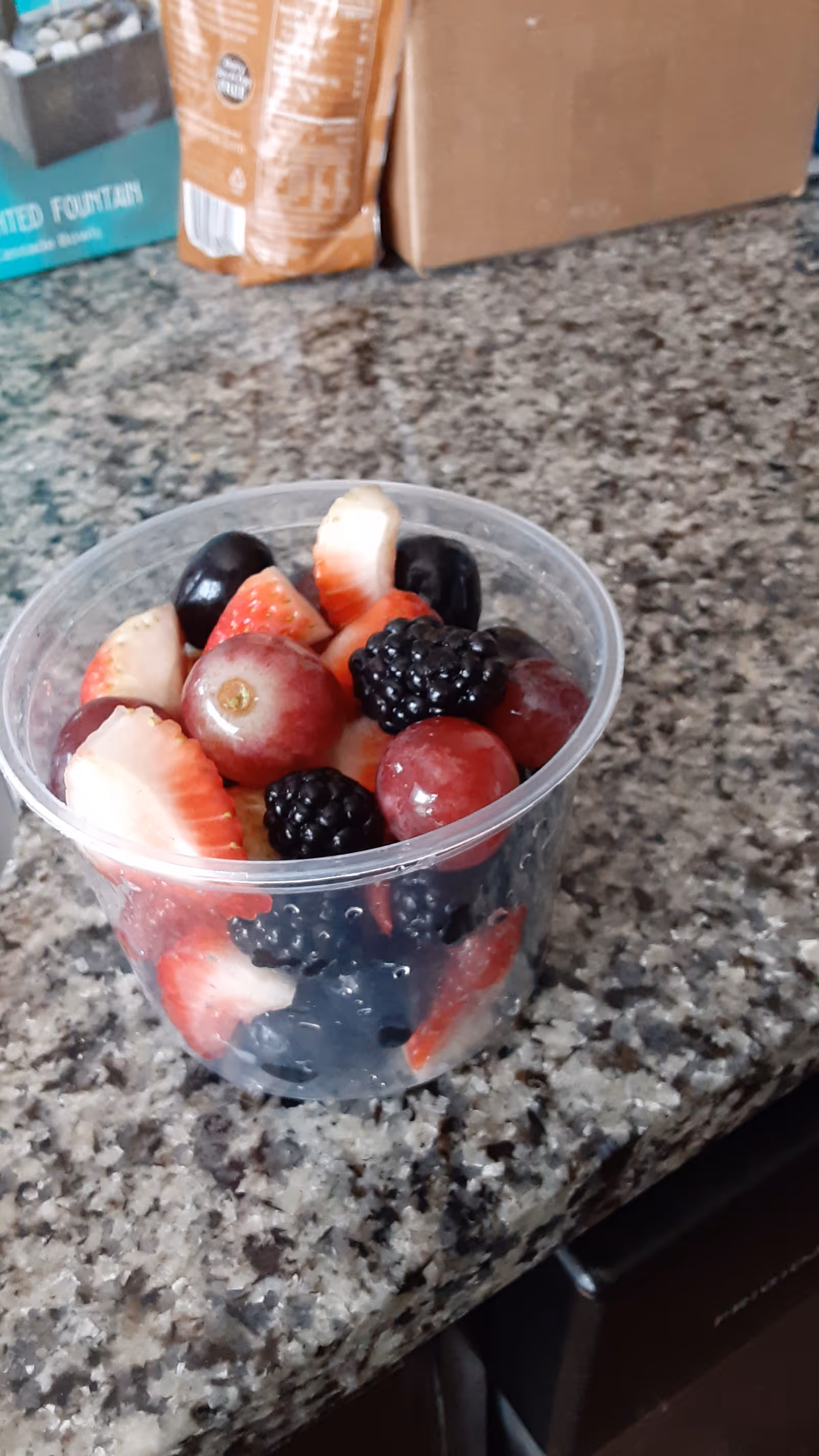 Clear plastic cup of mixed berries sits on a granite kitchen counter.