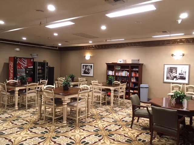Spacious indoor dining and common area with multiple tables, chairs, plants, and a bookshelf.