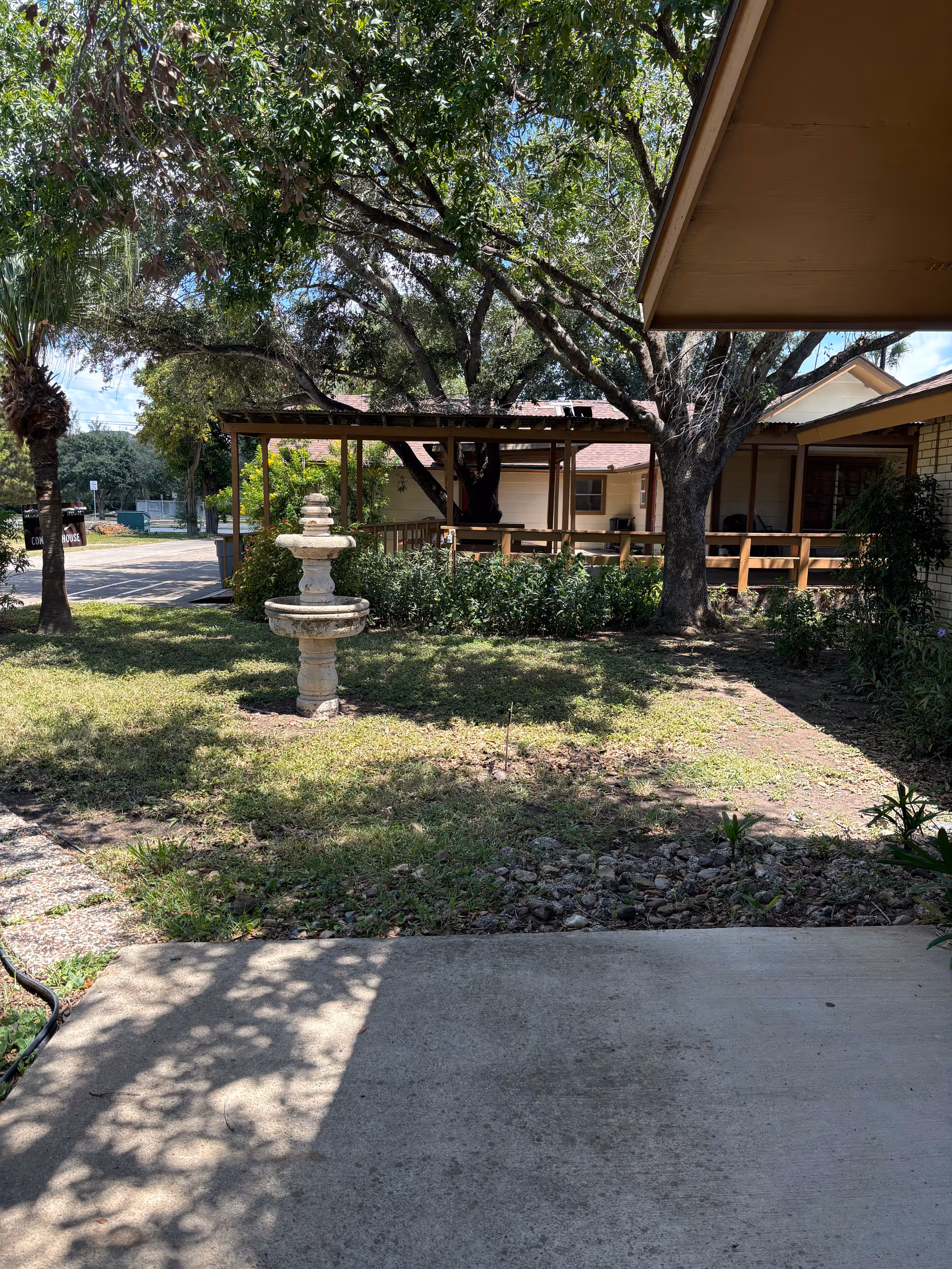 Outdoor view of a courtyard with trees, a fountain, and a covered porch.