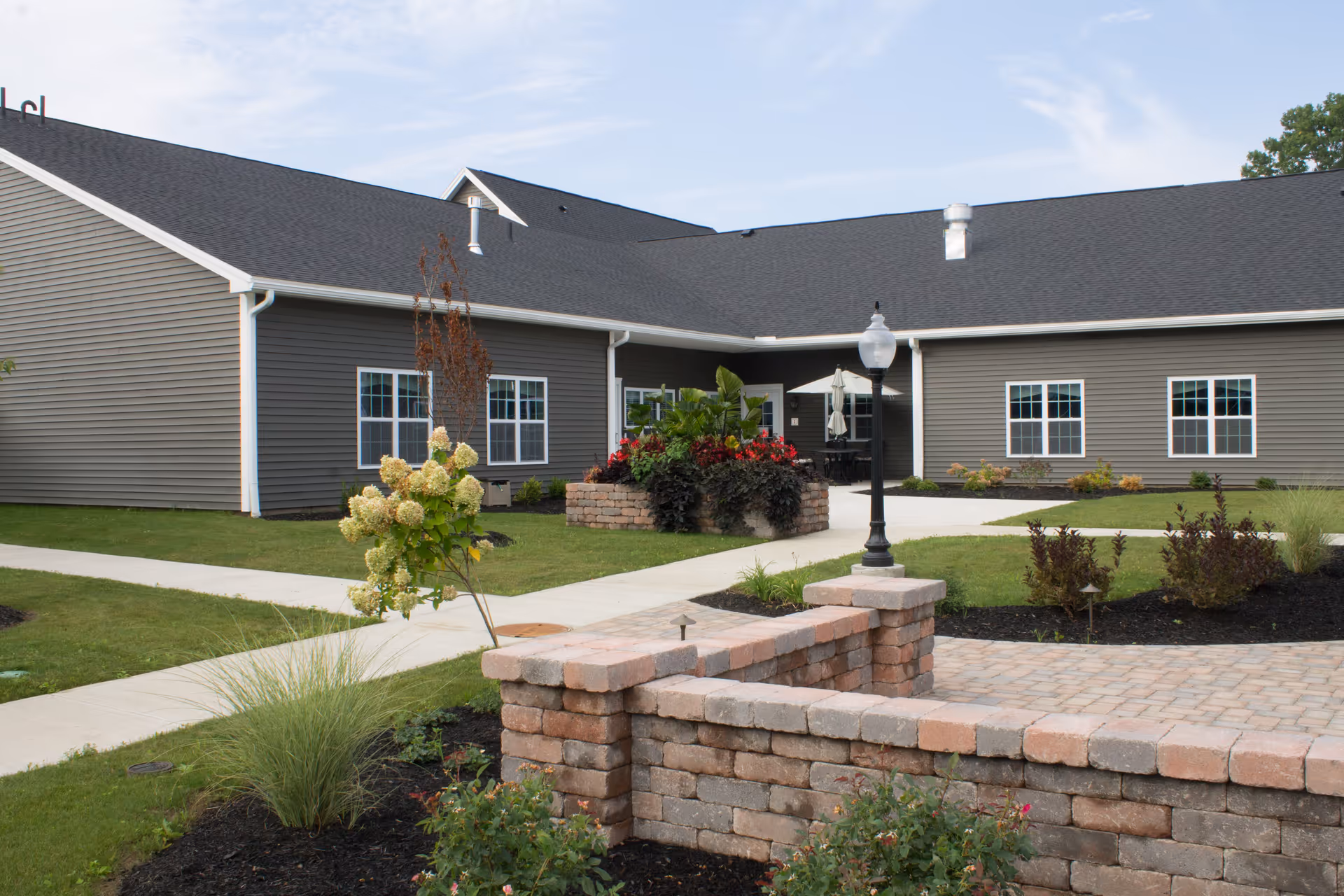 Single-story senior living facility exterior with brick courtyard wall and landscaping.