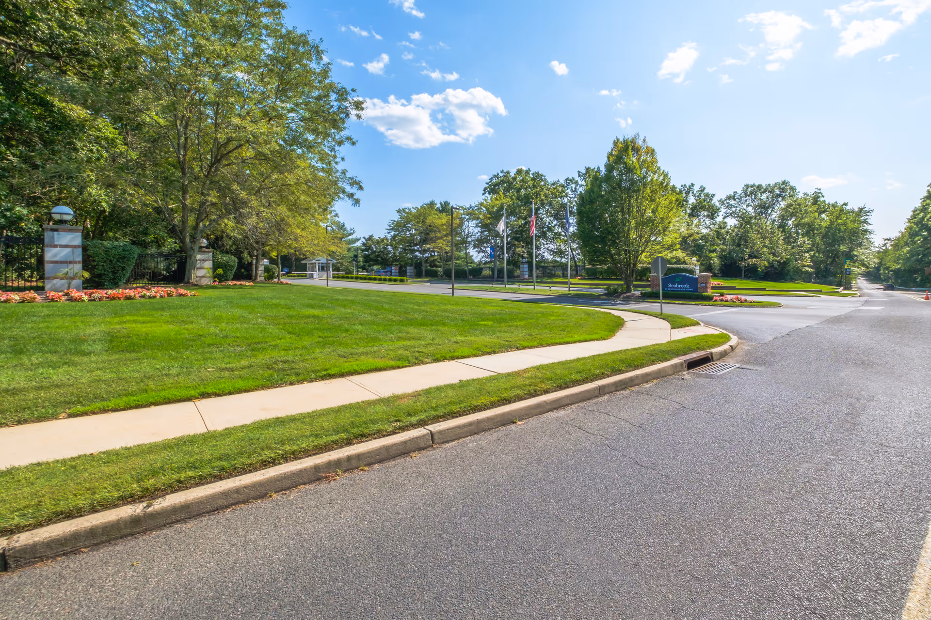 Tree-lined entrance drive and manicured lawn with a Seabrook sign by the sidewalk under a blue sky.