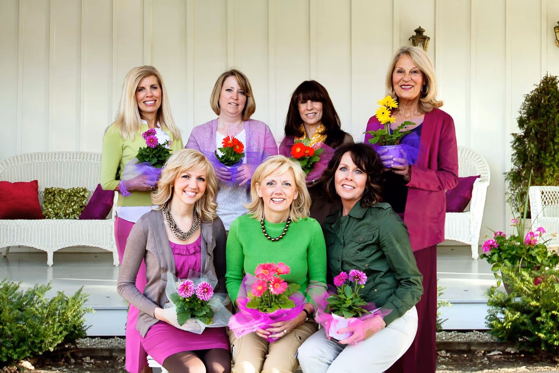 Group of caregivers and residents pose with flowers on a sunny porch.
