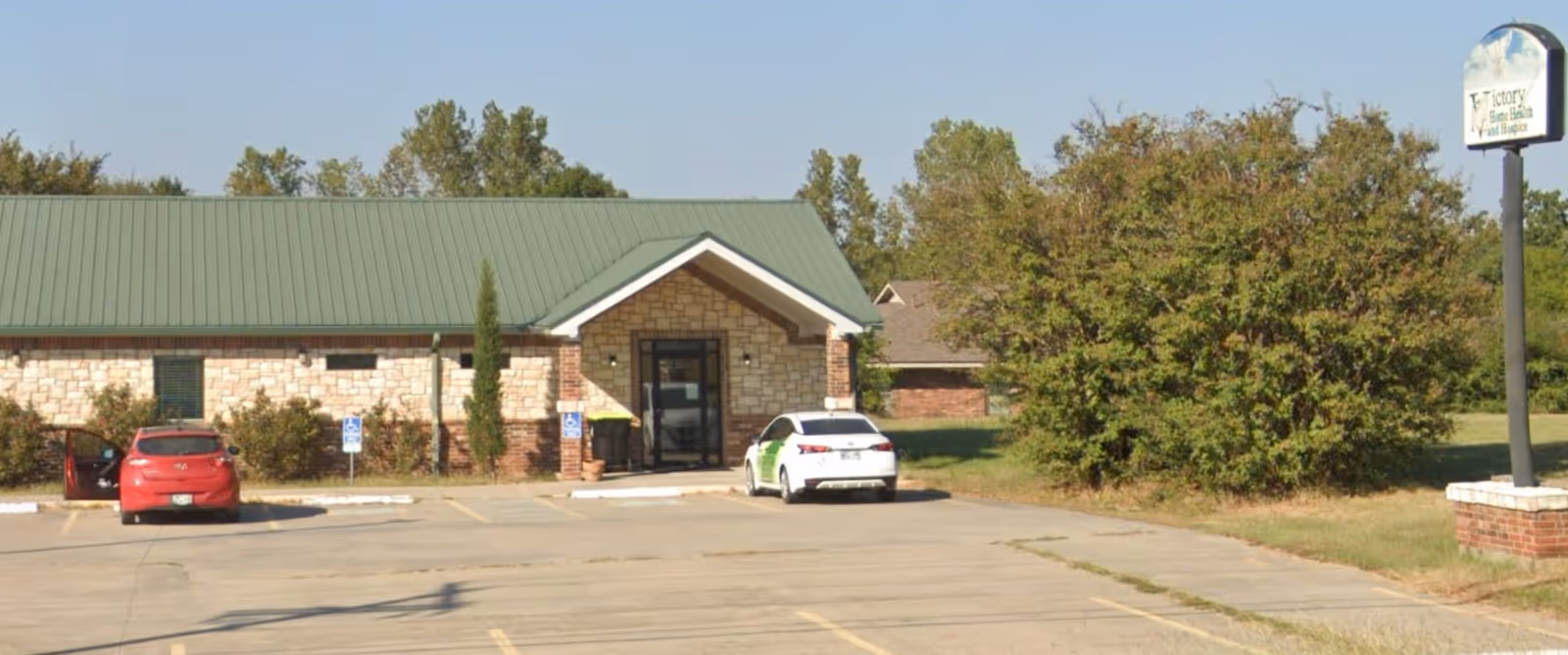 Exterior view of a stone-brick building with green roof and Victory Home Health Hospice sign.