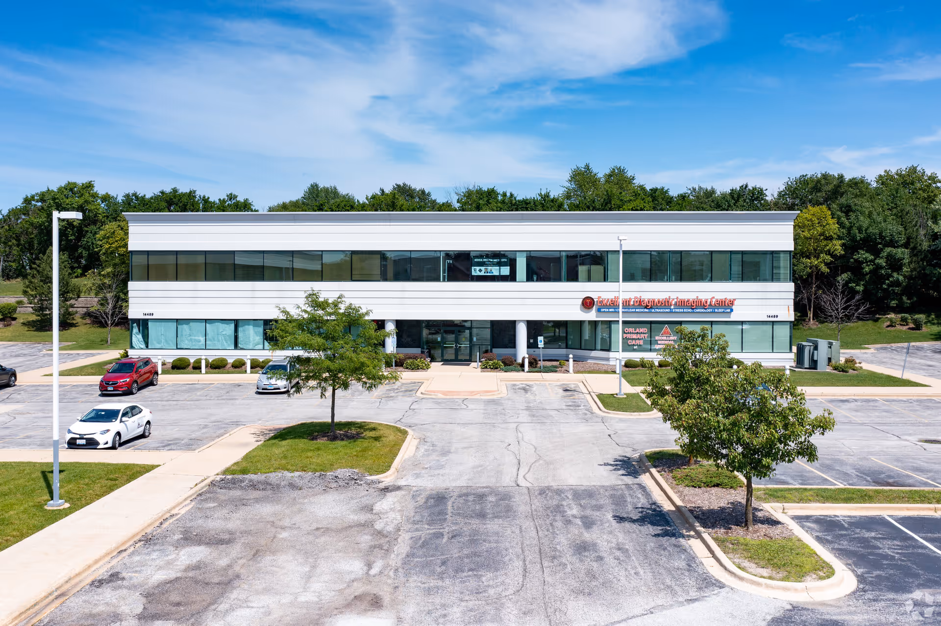 Two-story modern medical building with glass windows and a spacious parking lot in front.